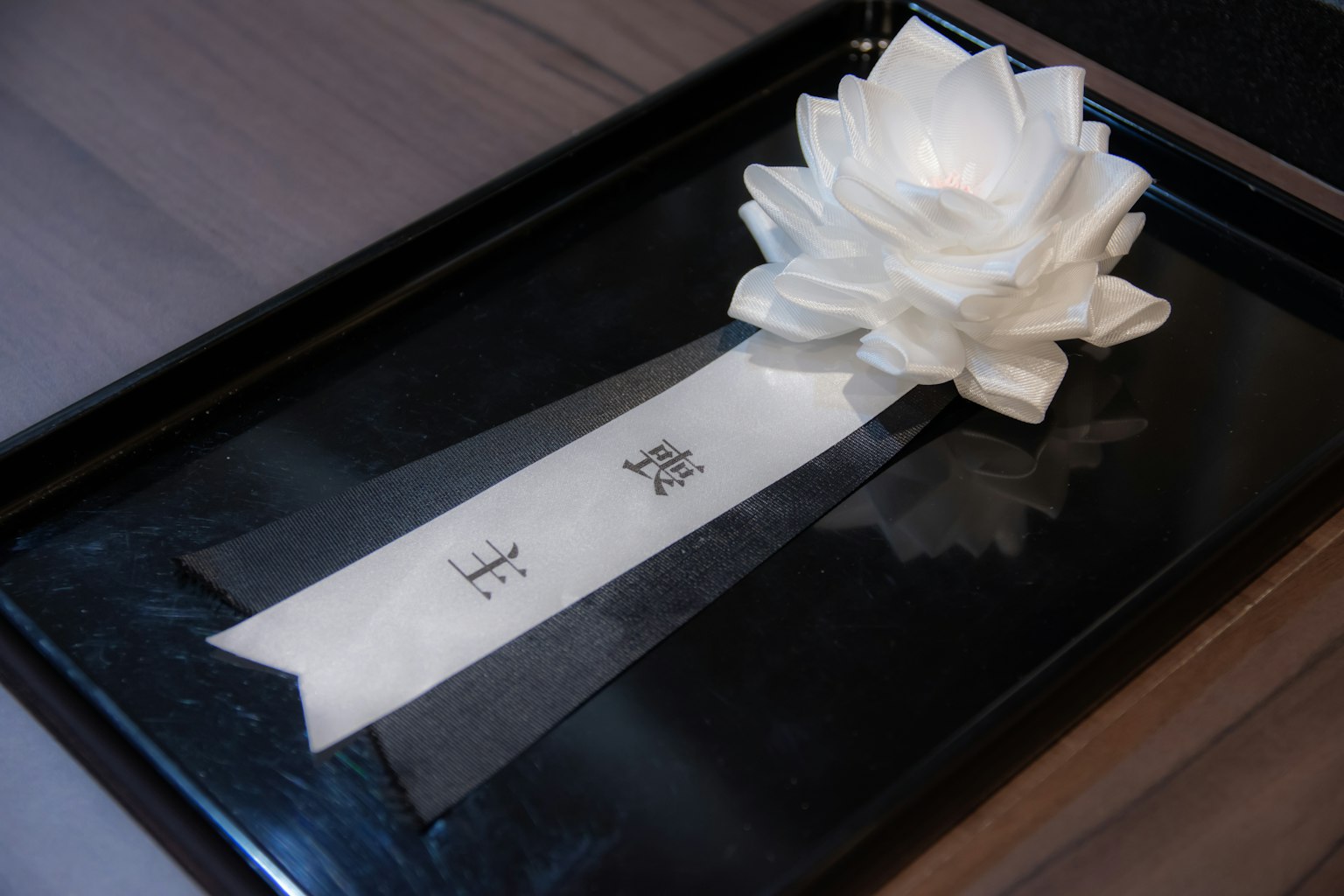一個白色花朵裝飾和絲帶放在黑色托盤上