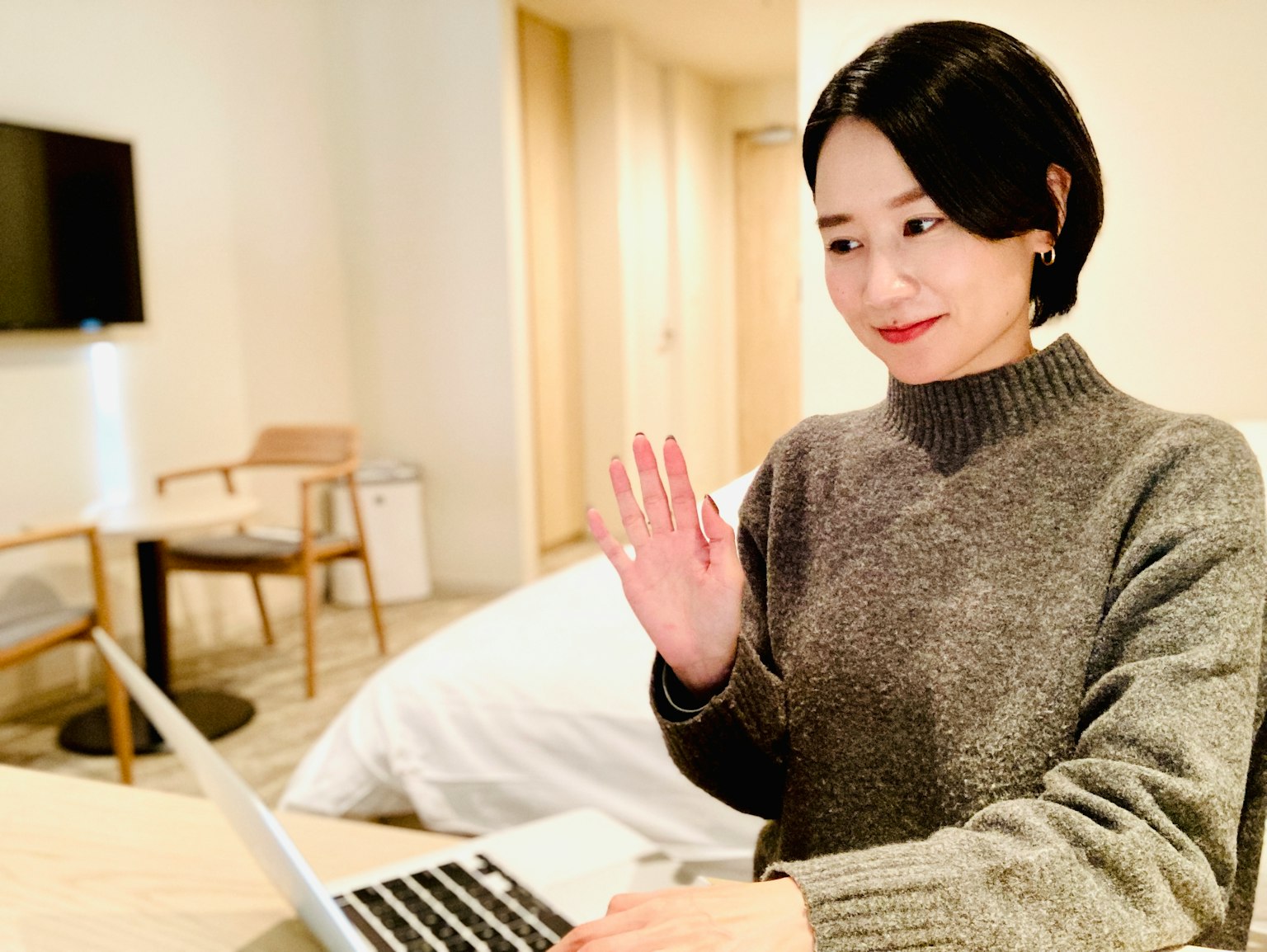 一位女性在舒适的房间里用笔记本电脑工作时挥手