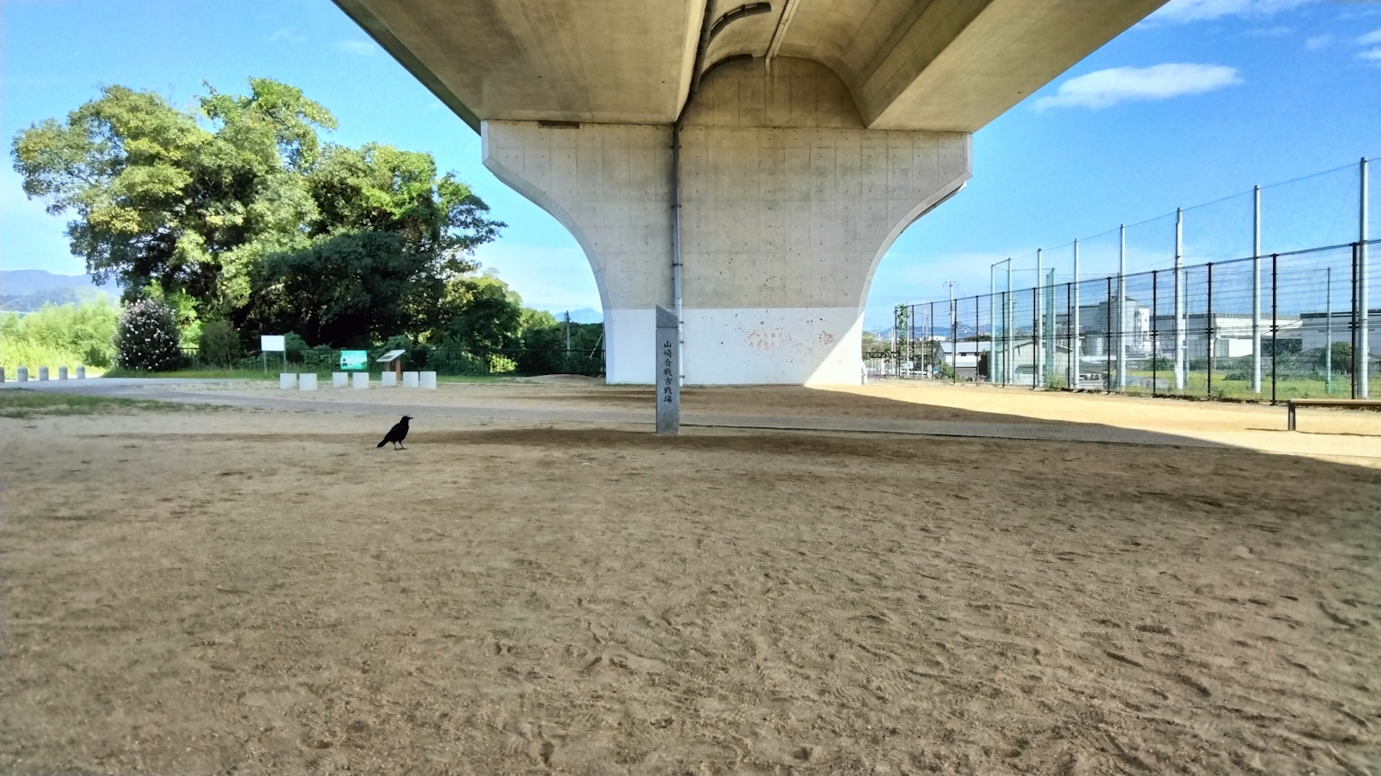 Un'area sabbiosa sotto un ponte con cielo blu e alberi sullo sfondo