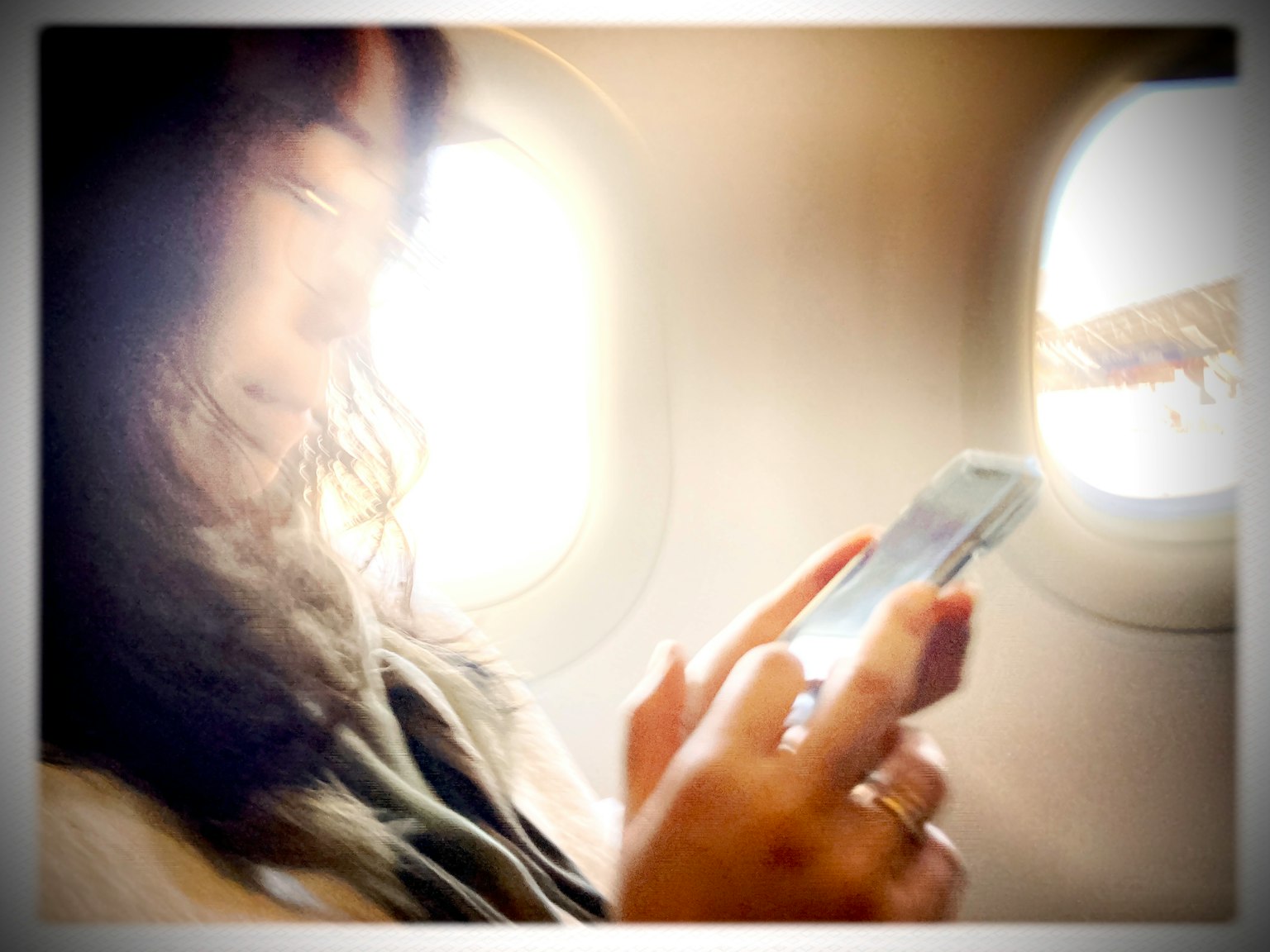 飛行機の窓の近くでスマートフォンを操作する女性