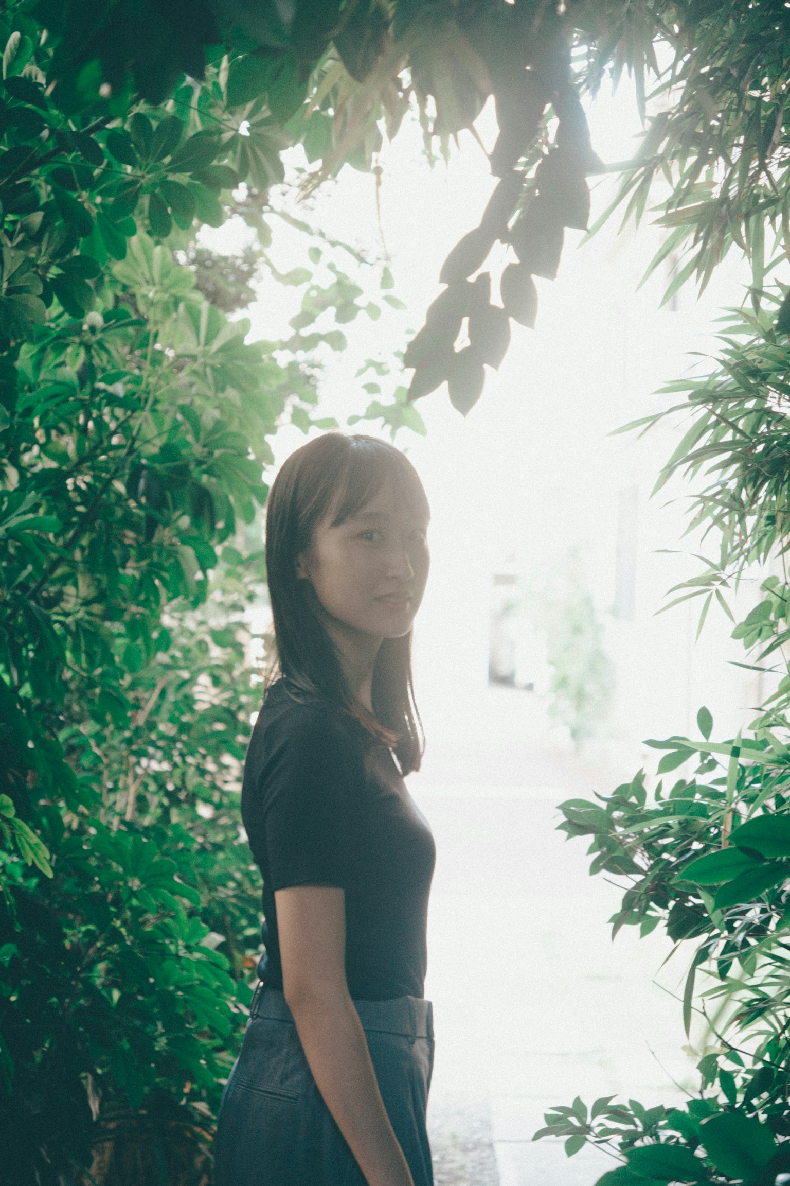 Une femme se tenant parmi des plantes vertes avec une lumière douce en arrière-plan