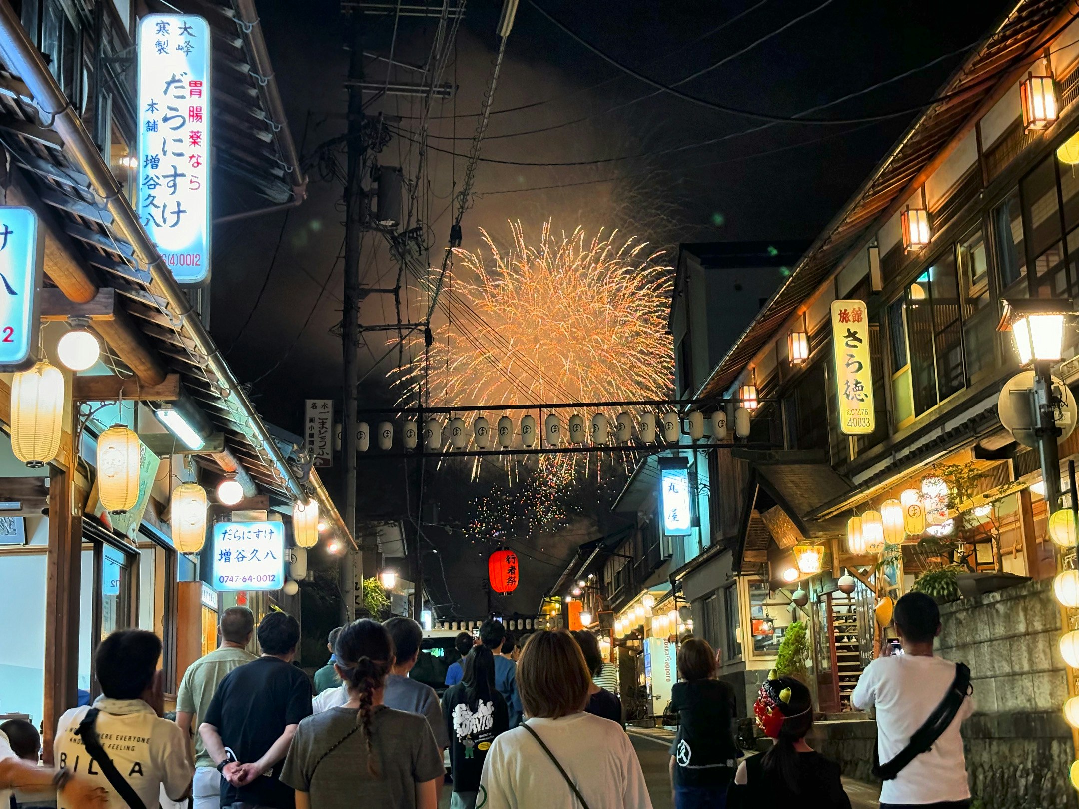 提灯と屋台のある夜の路地で花火が上がる宿場の風景