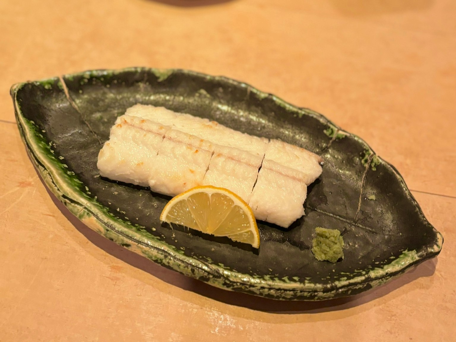 Weißer Fischsashimi auf einem grünen Teller mit Zitrone und Wasabi