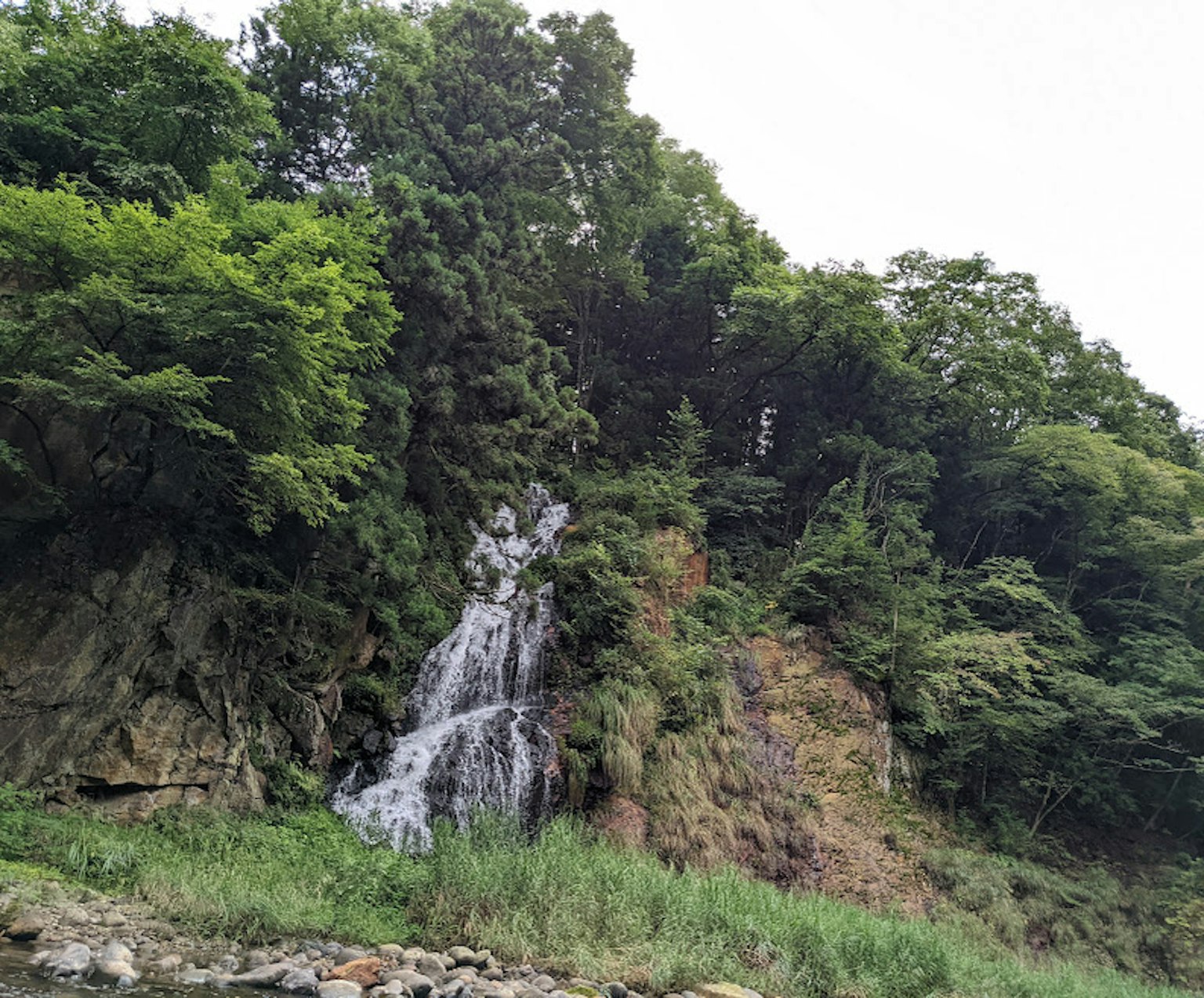 Ein kleiner Wasserfall, der von einer felsigen Klippe umgeben von üppigem Grün herabfließt