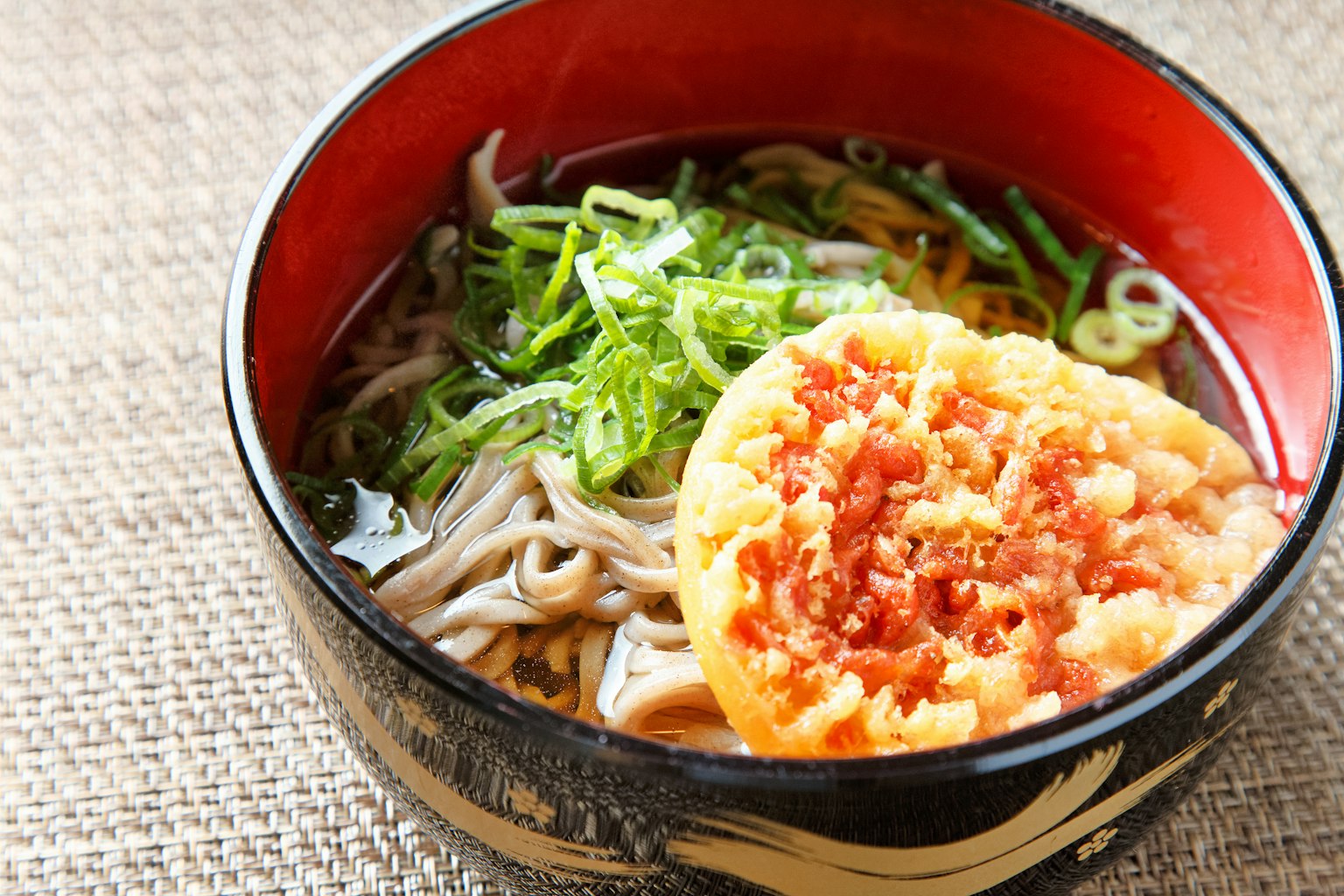 Noodles soba in una ciotola rossa guarniti con cipollotti e tempura