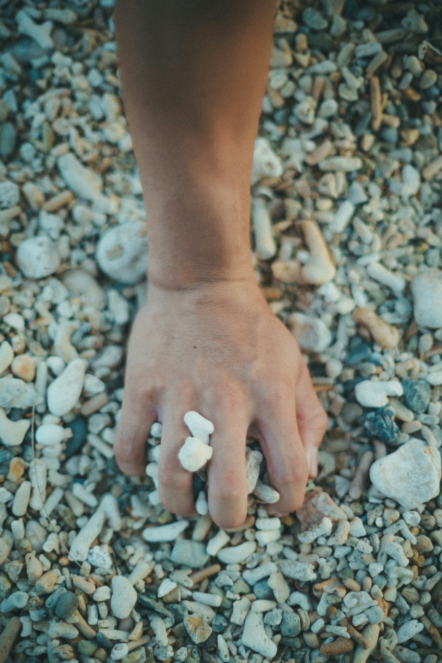 A hand reaching through gravel with small stones