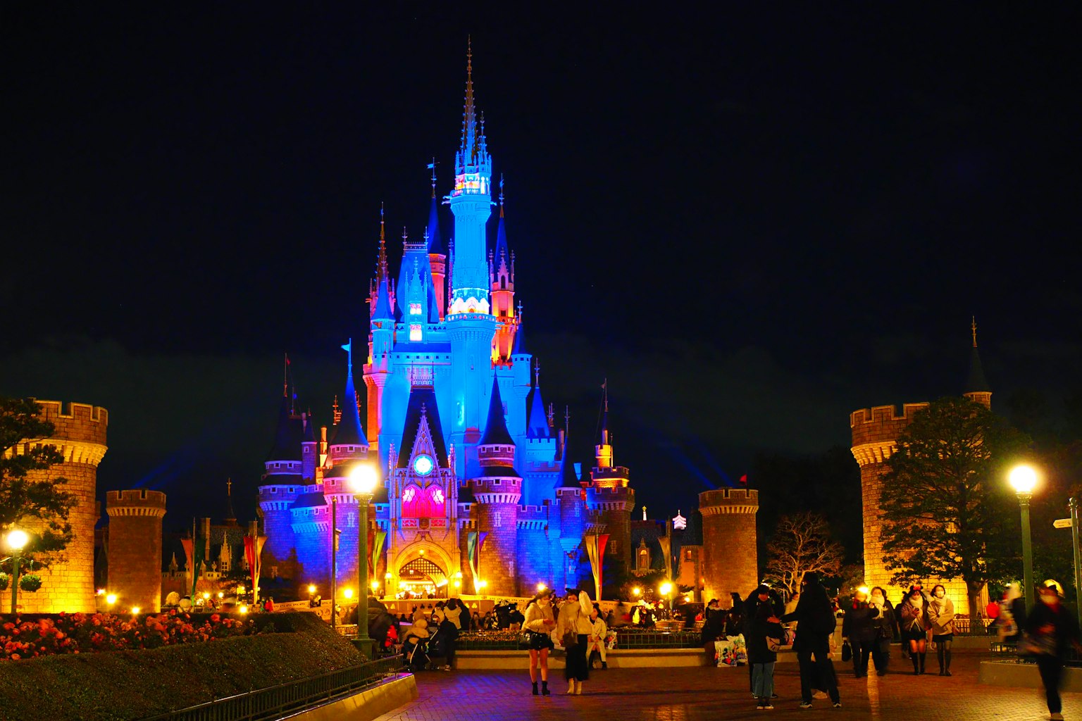 Castillo de Cenicienta iluminado en azul y naranja por la noche en un parque Disney