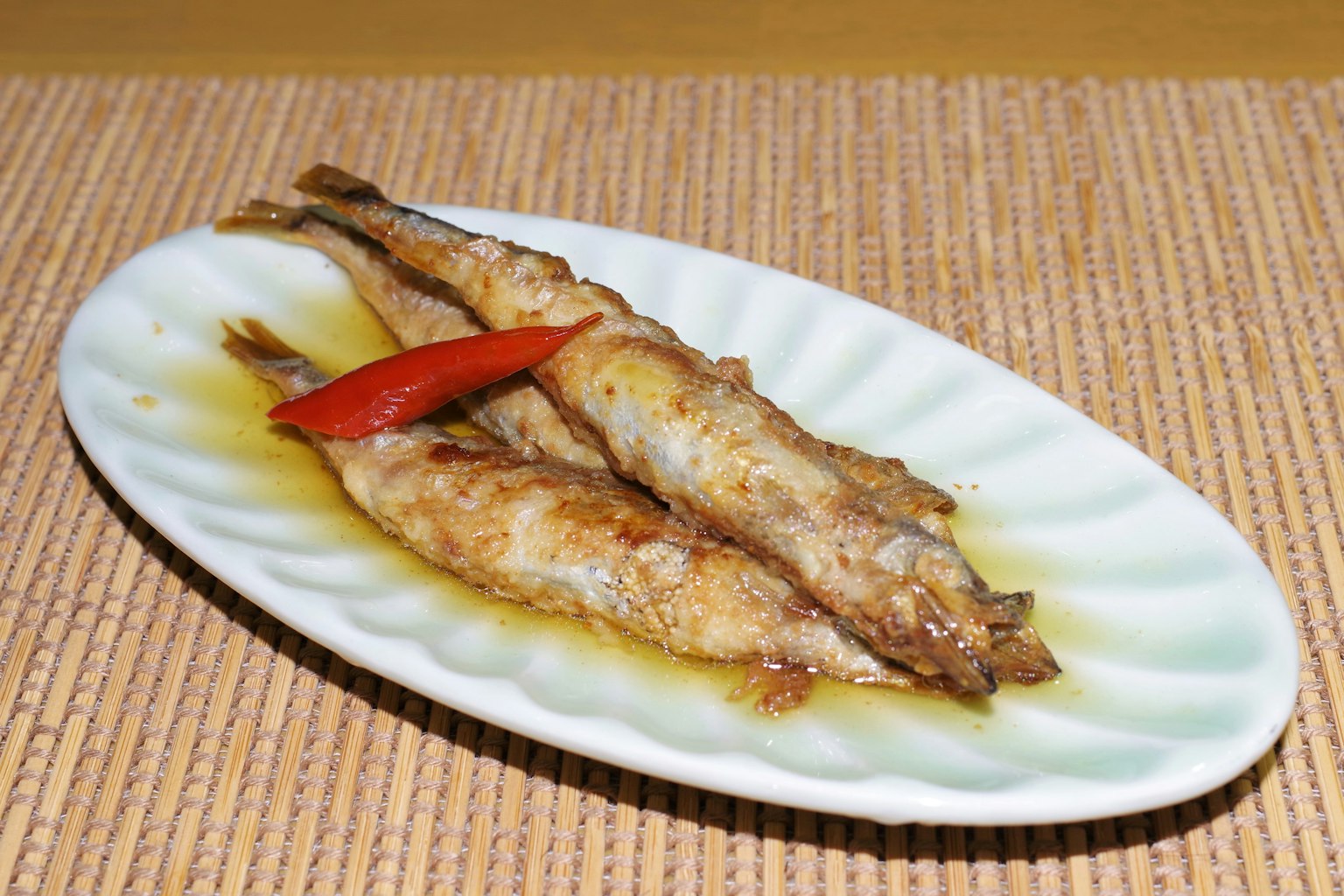 Ikan bakar disajikan di piring putih dengan irisan cabai merah