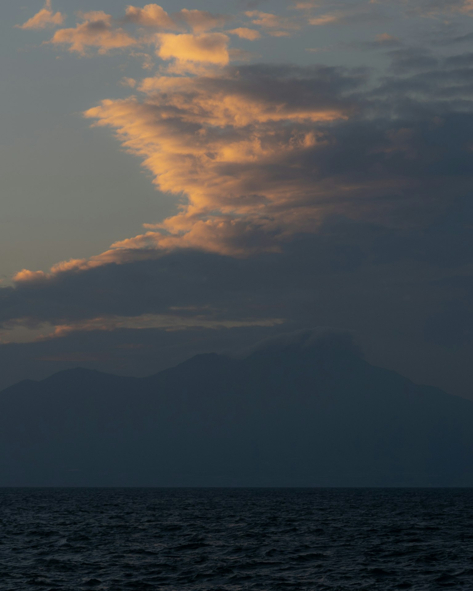 Silueta de montañas y nubes sobre el mar al atardecer