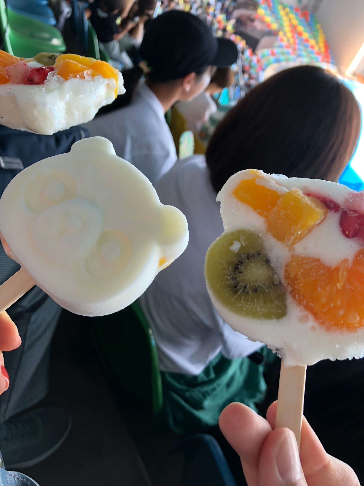 Zwei bunte Eis am Stiel, die von Händen mit Obsttoppings gehalten werden