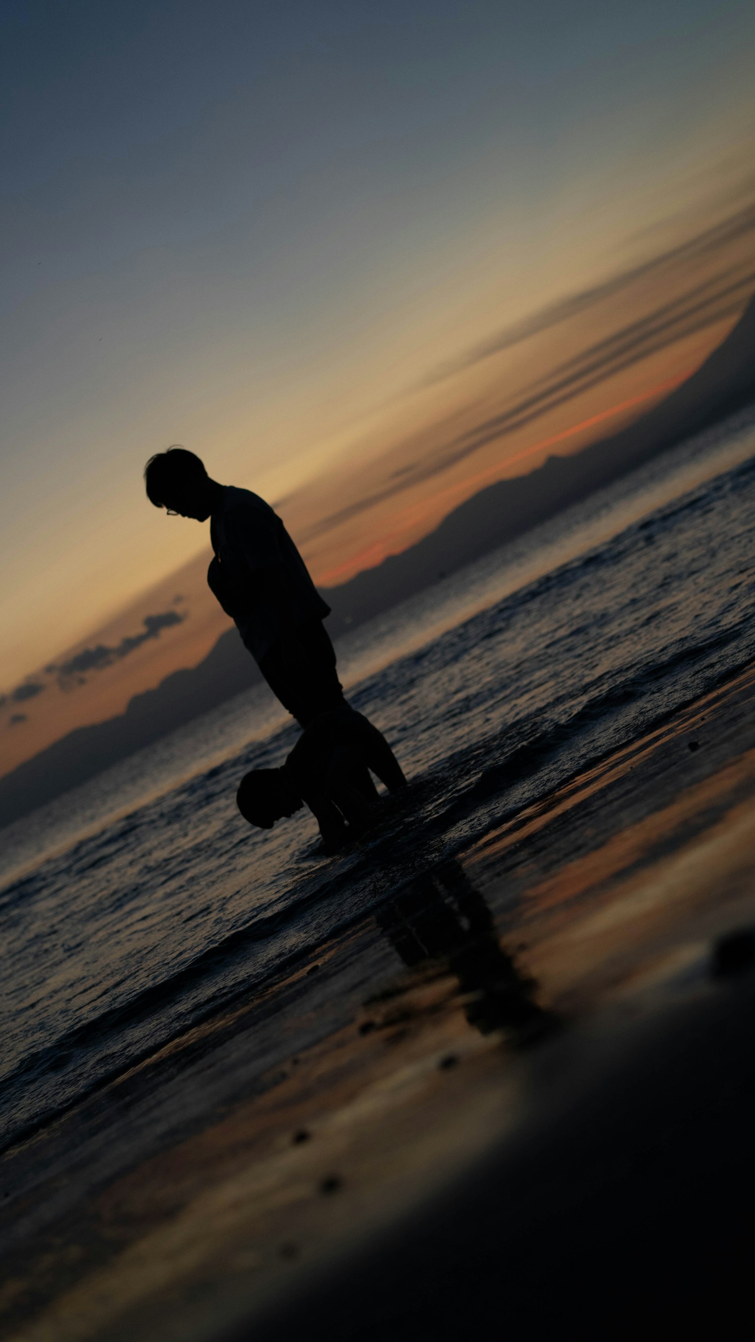 Siluet seseorang berjalan di pantai saat matahari terbenam