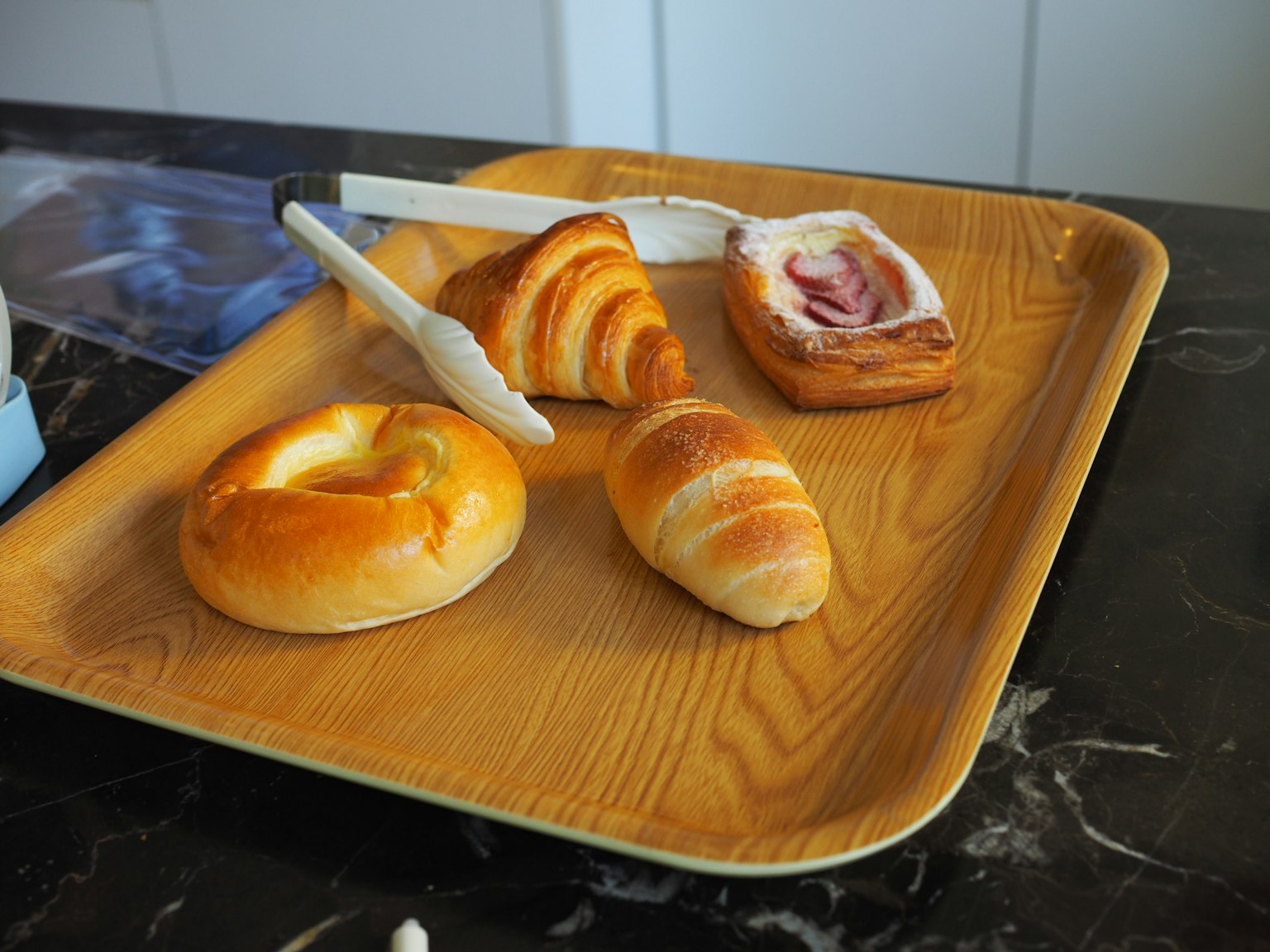 Assorted baked pastries and bread arranged on a wooden tray