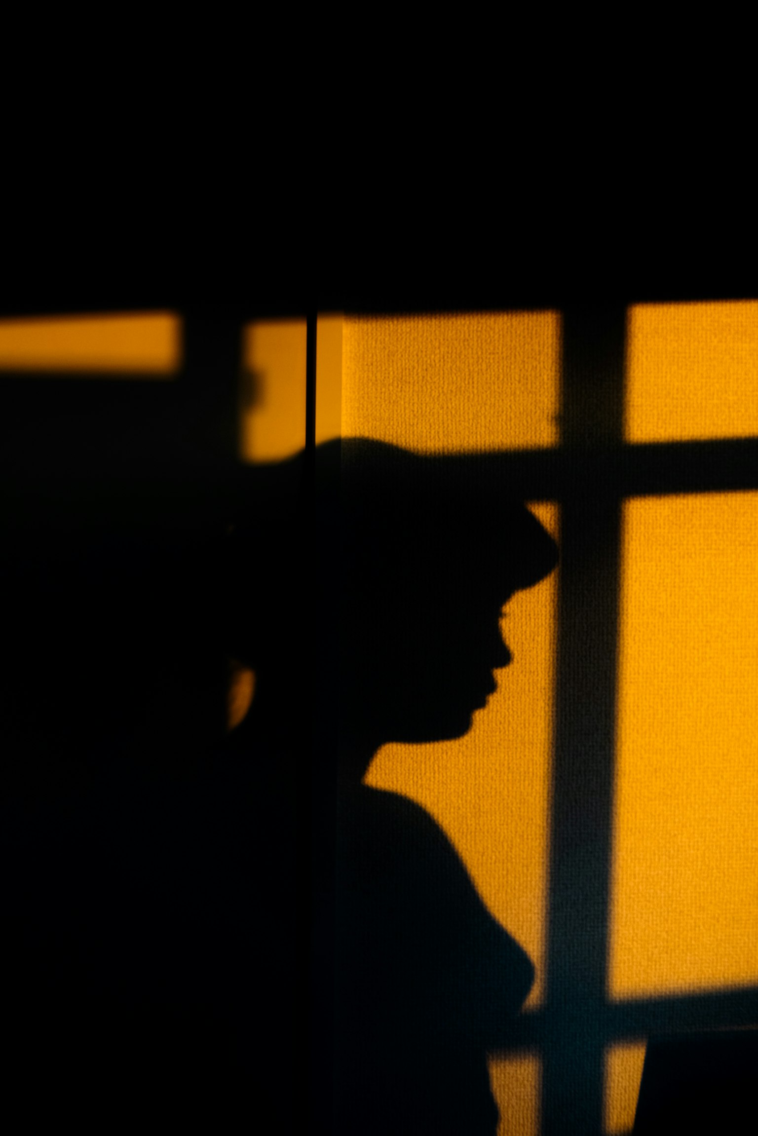 Silhouette di una persona con luce arancione che filtra da una finestra