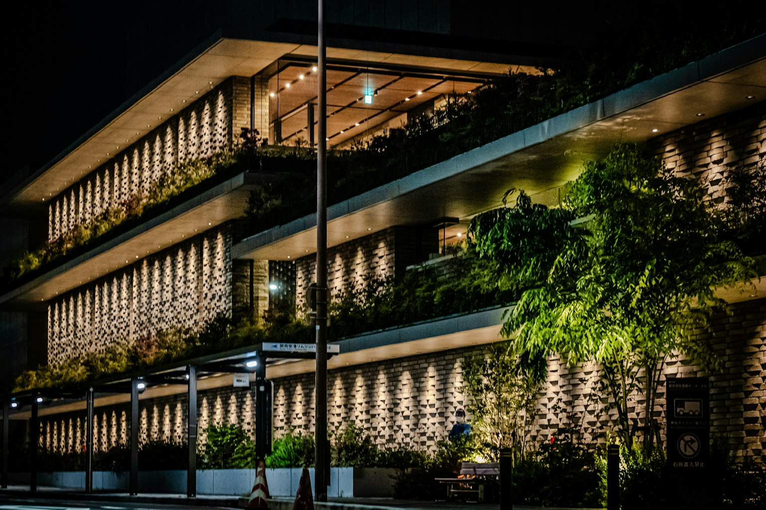 現代建築外觀在夜間美麗照亮，帶有豐盛的陽台植物和石牆