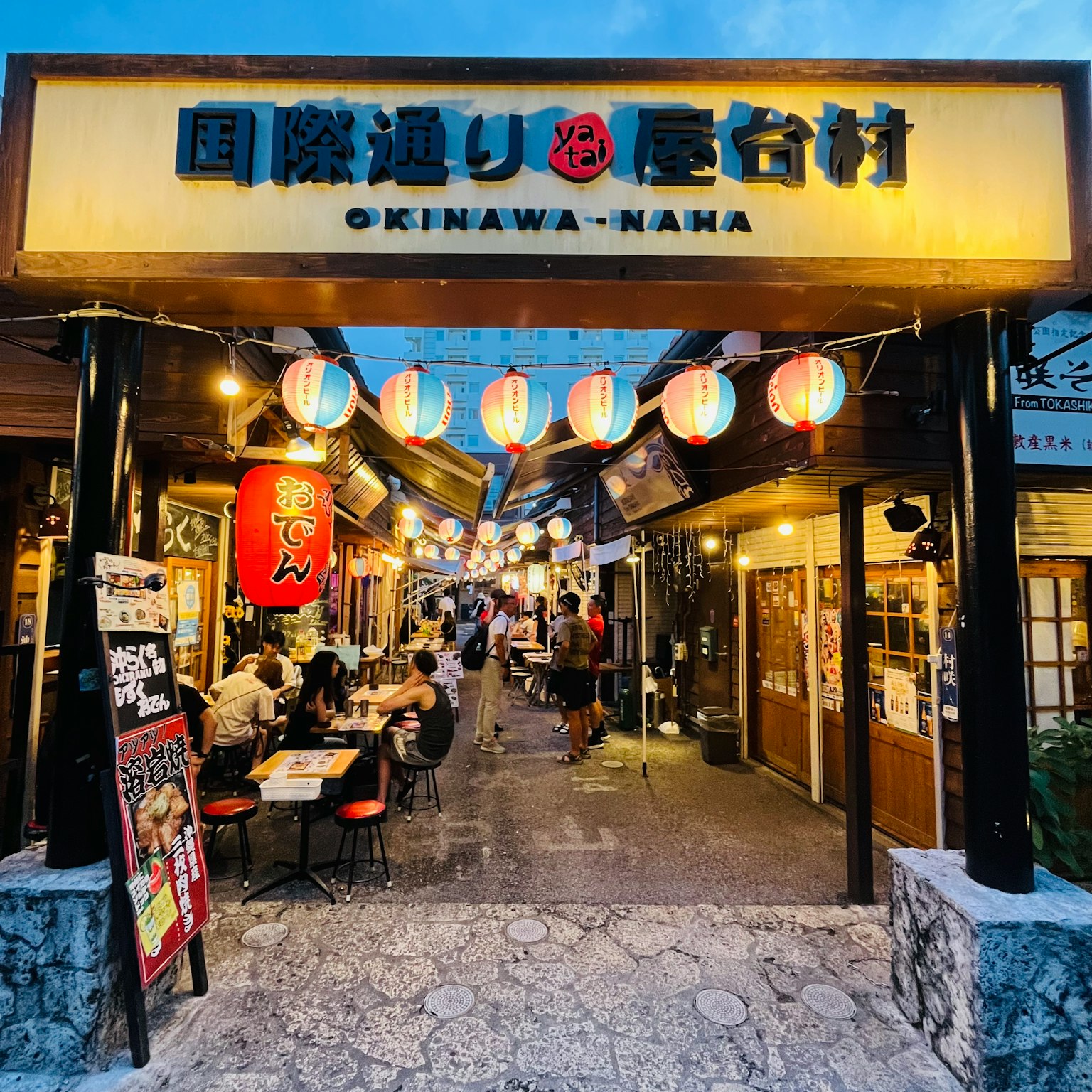 ทางเข้าหมู่บ้านอาหารโอกินาว่า-นานะที่มีป้ายสว่างและโคมไฟ