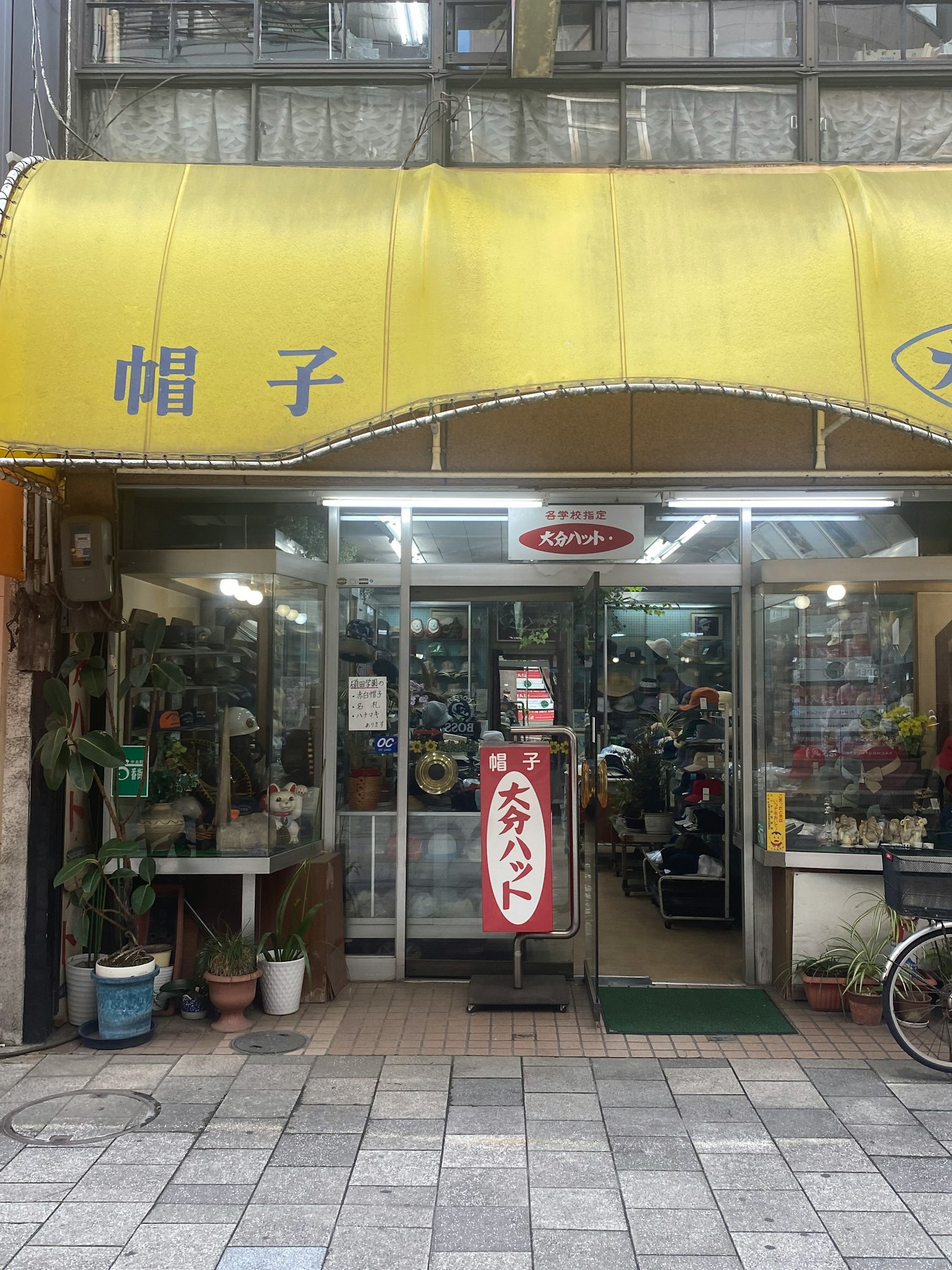 Entrance of a yellow awning hat shop with various items visible inside