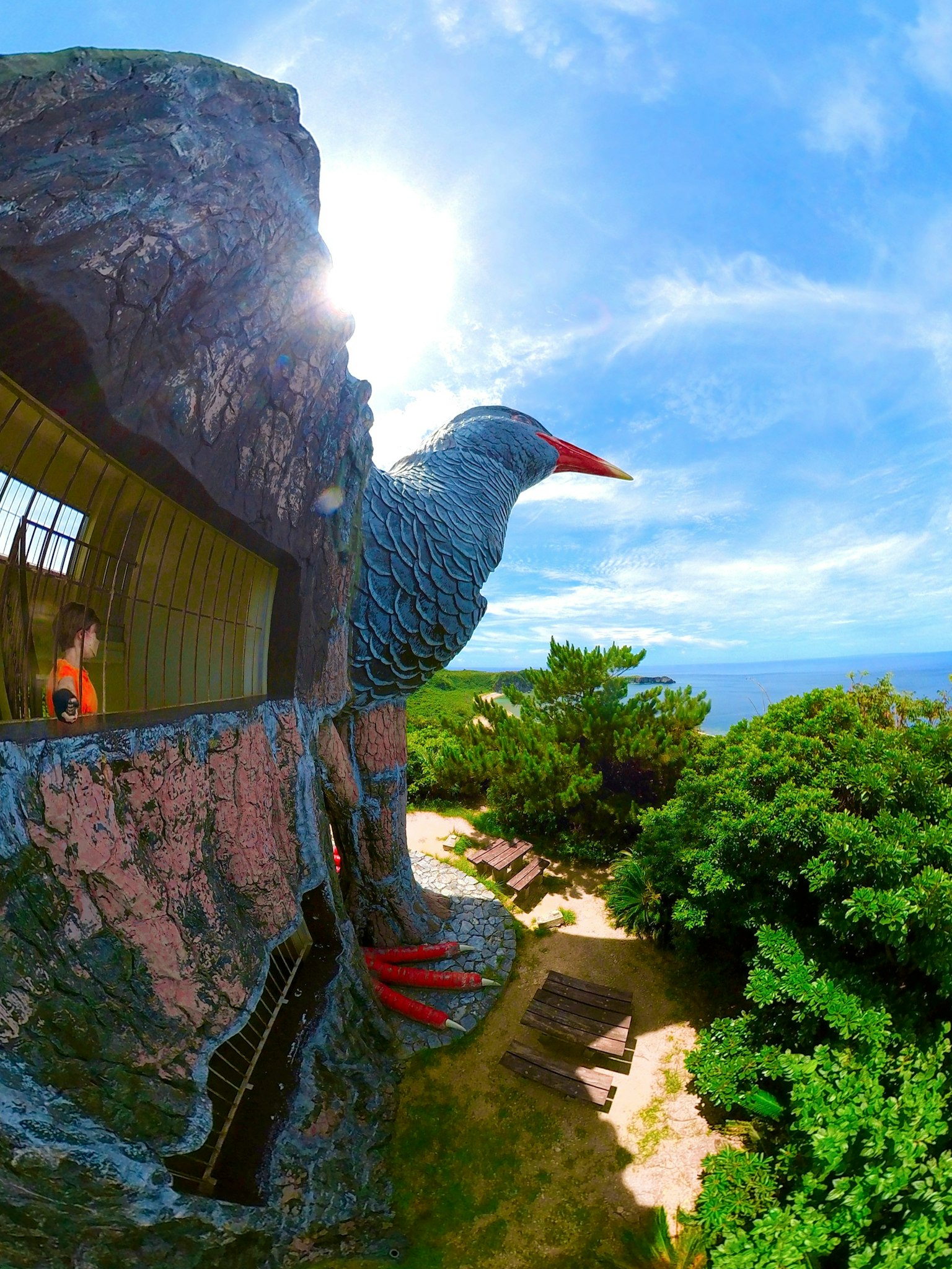 Grande sculpture d'oiseau surplombant un beau paysage avec ciel bleu et arbres verts