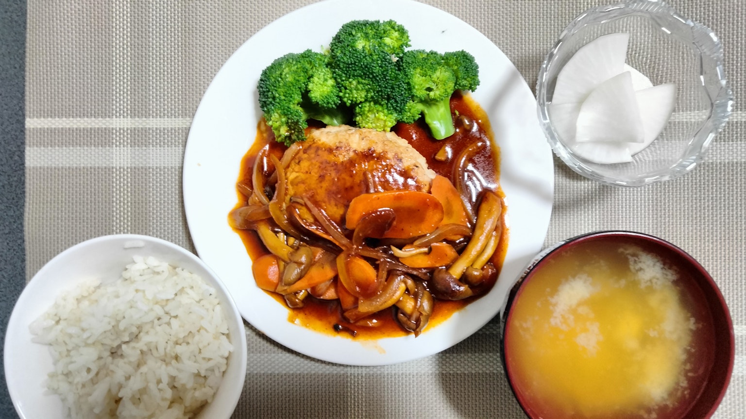 Un piatto con riso, pollo in salsa, broccoli, zuppa di miso e un uovo