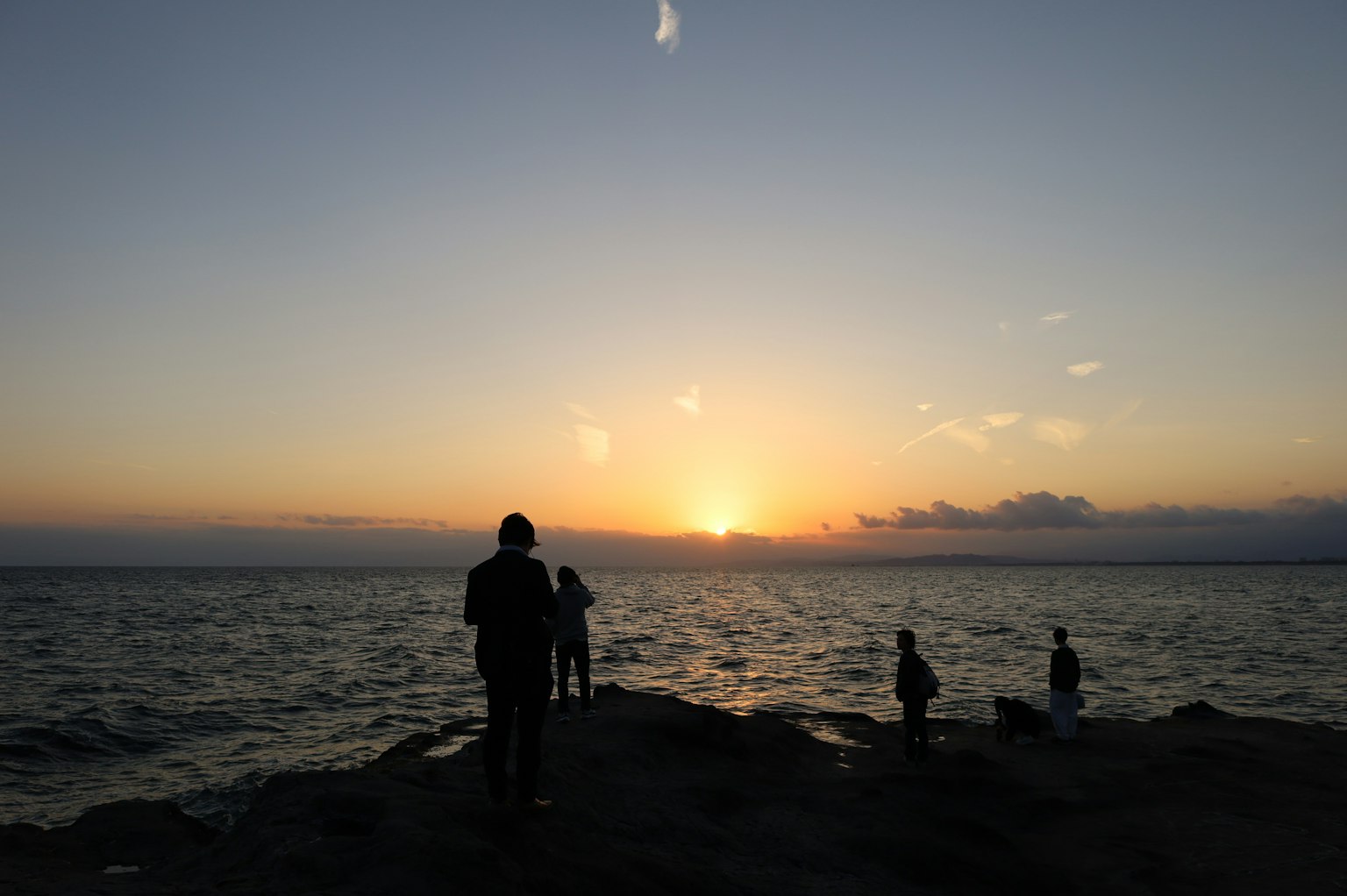 夕日を背景に海辺に立つ人々のシルエット