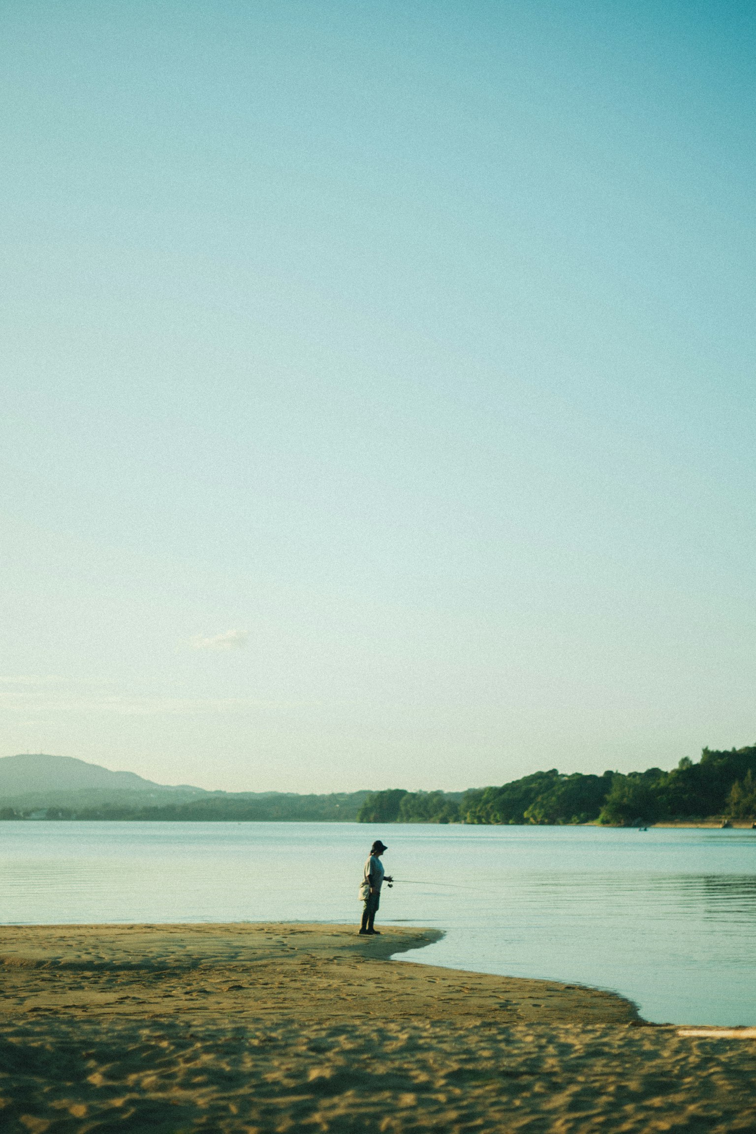 静かな湖のほとりに立つ人影と穏やかな空の風景