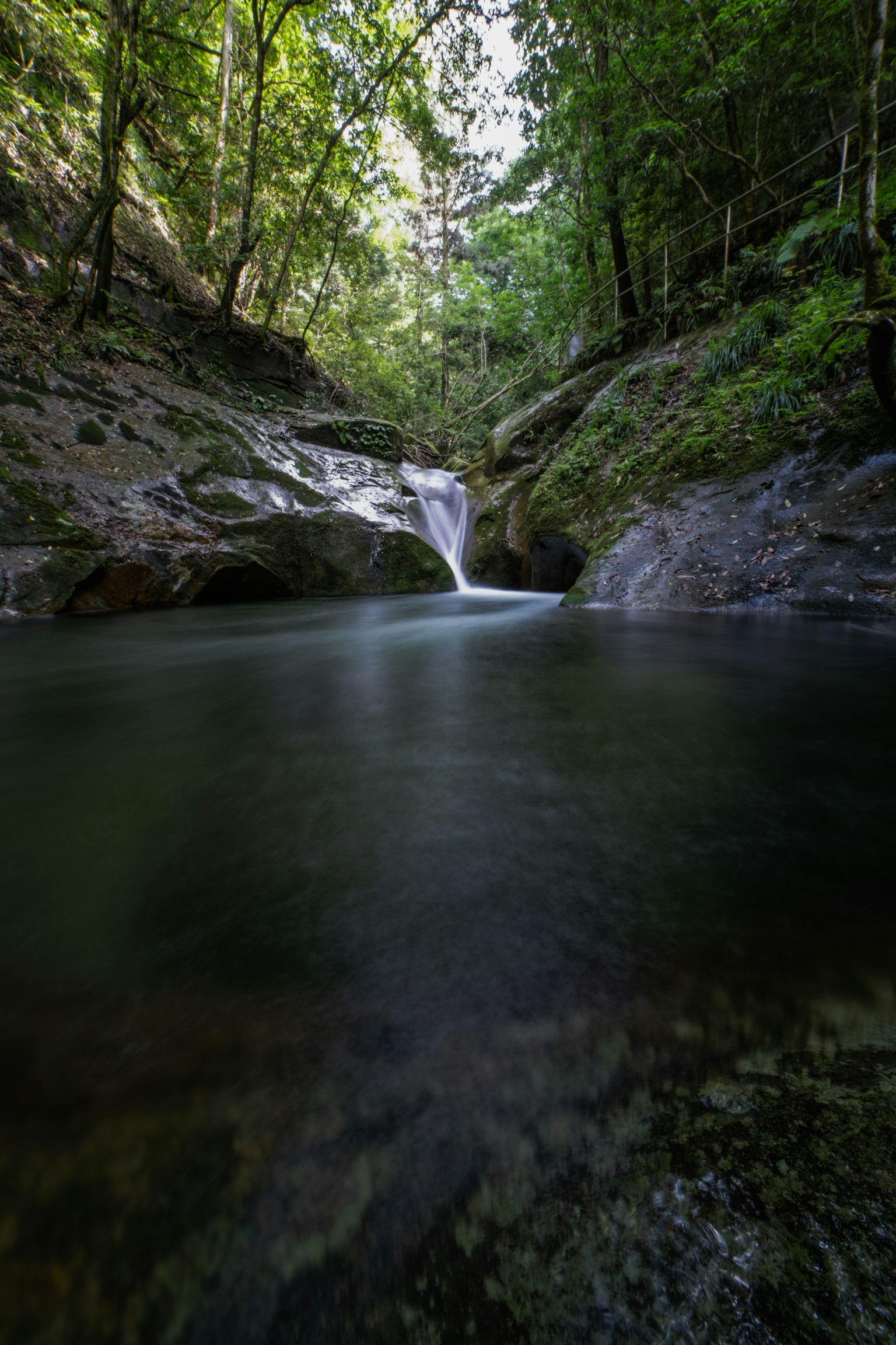 Air terjun tenang dikelilingi hutan hijau subur dengan permukaan air yang reflektif