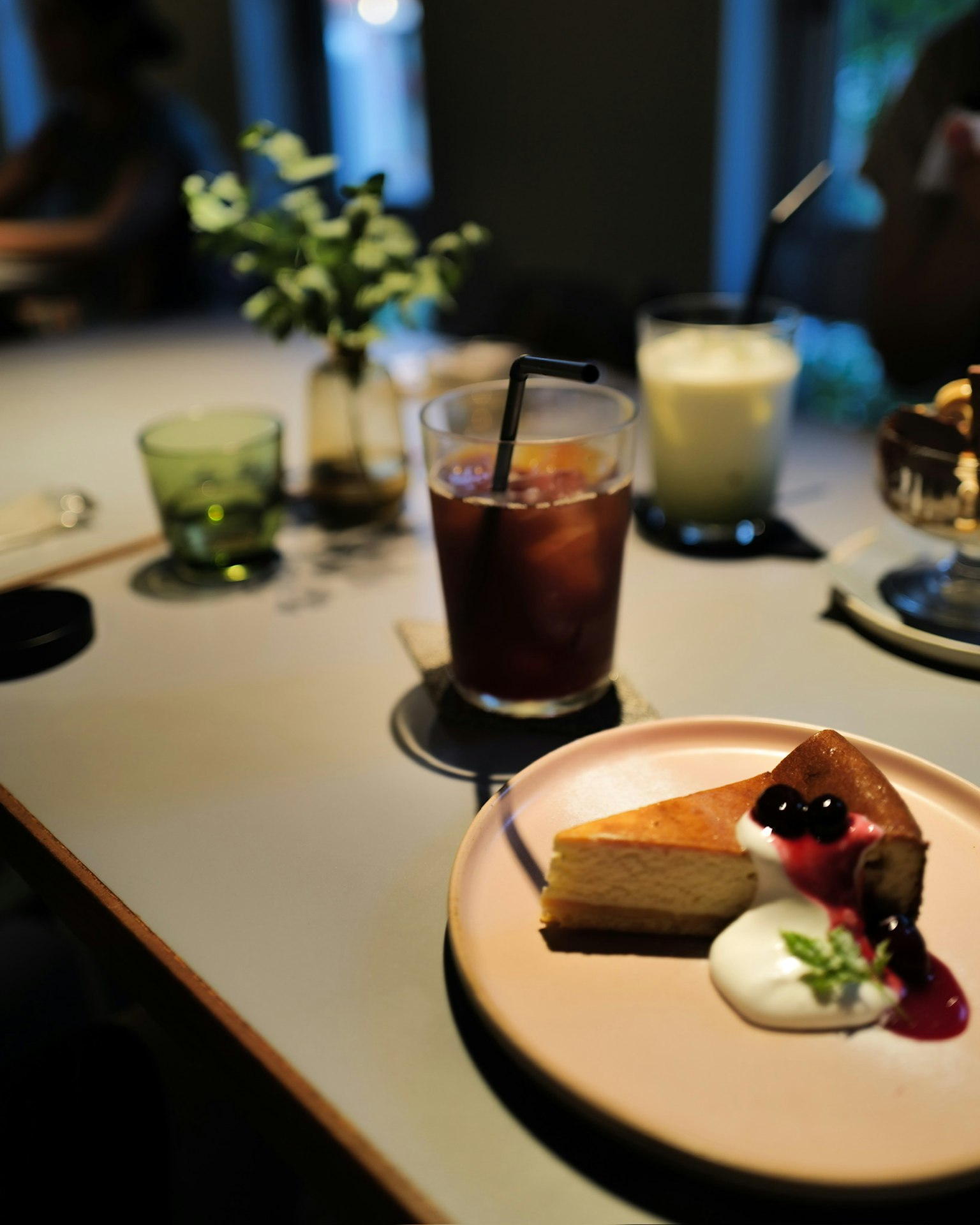 寧靜的咖啡館場景，桌上有起司蛋糕、奶油、飲料和綠色植物