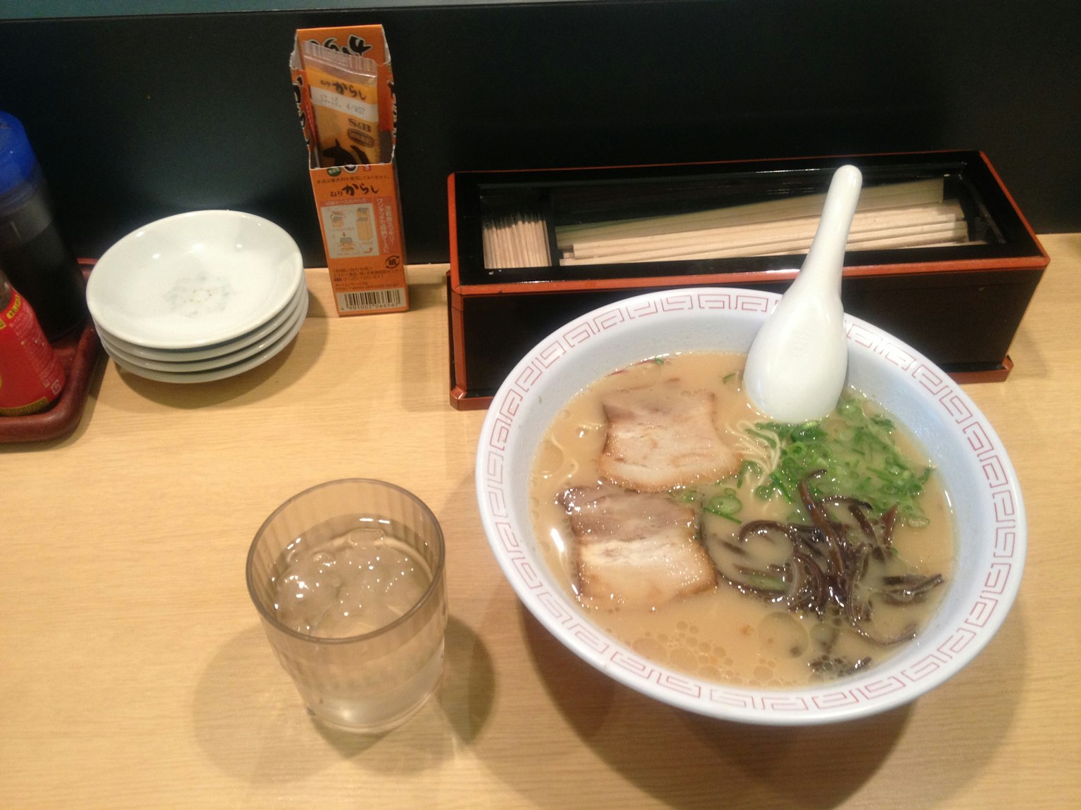 Un bol de ramen avec des tranches de porc et des légumes sur une table en bois avec un verre d'eau
