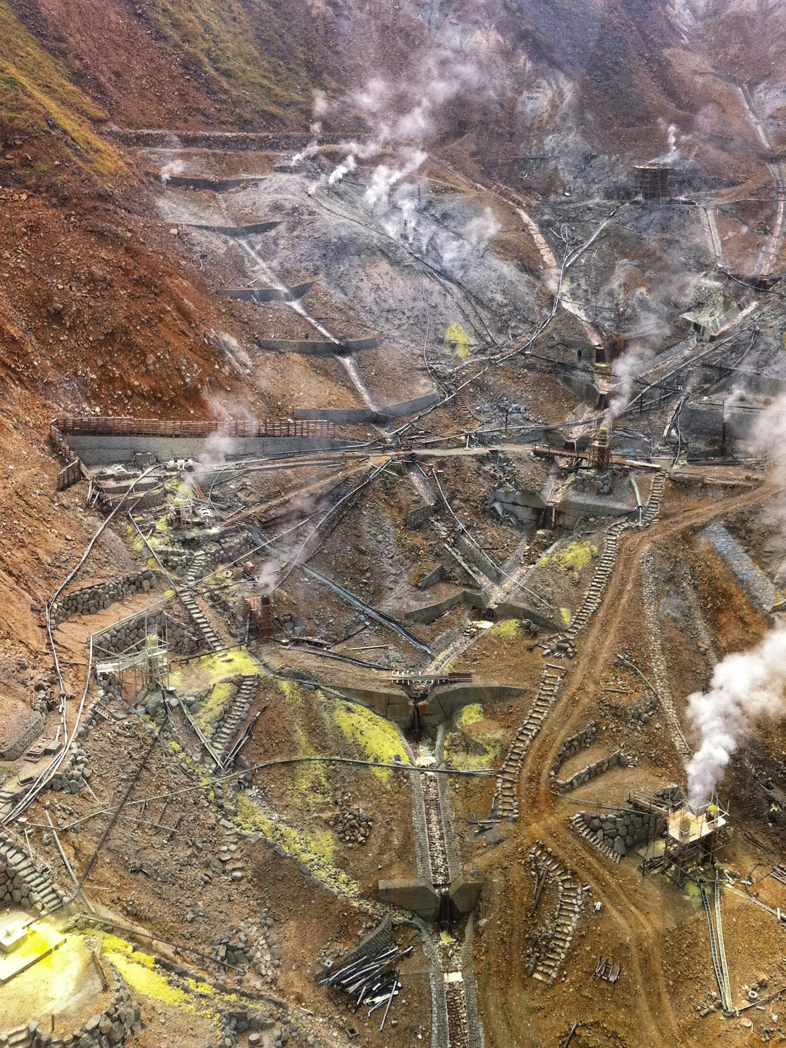 Vue aérienne d'un site minier avec des structures émettant de la fumée et des minéraux verdâtres