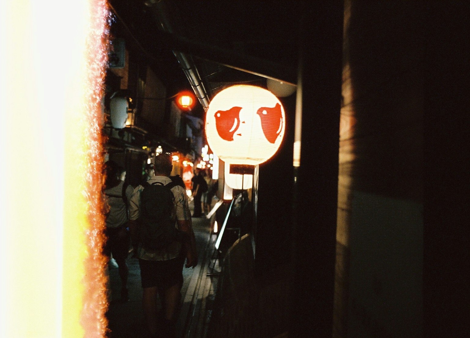 夜の街並みに浮かぶ赤い目の提灯と人々のシルエット