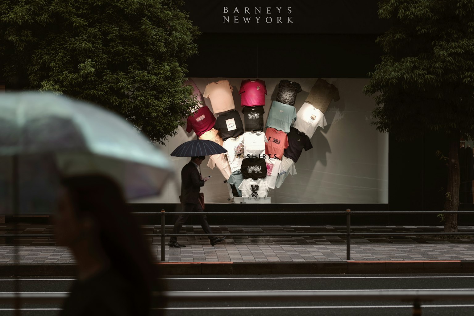 Una persona con un ombrello che passa davanti a una vetrina con borse colorate