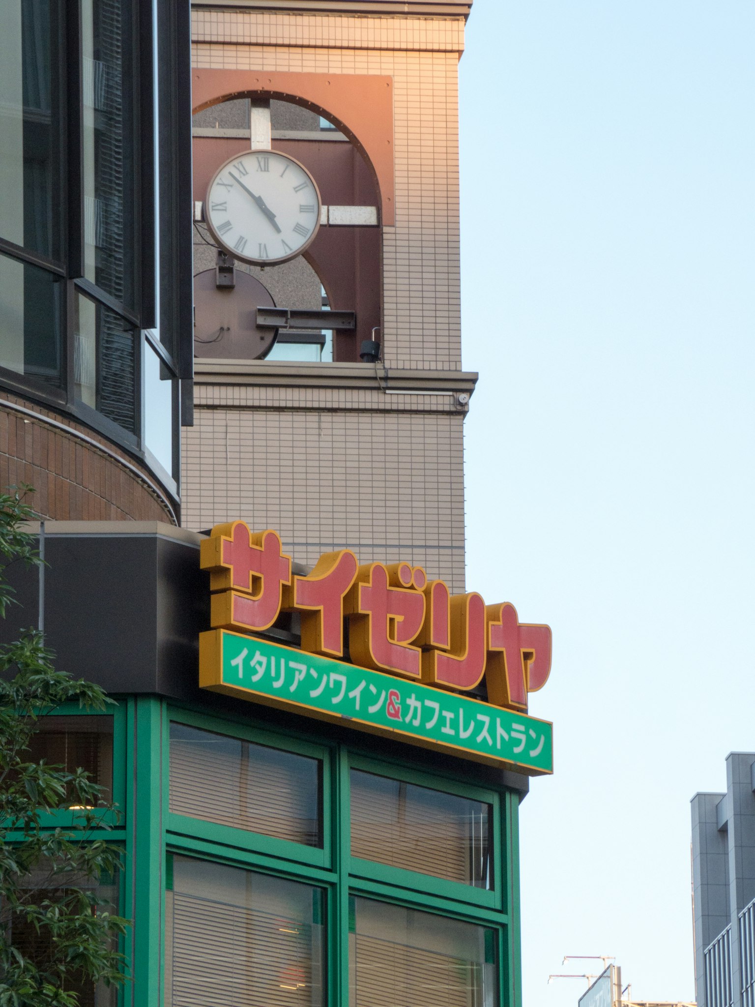 Cartel del restaurante Saizeriya con una torre del reloj al fondo