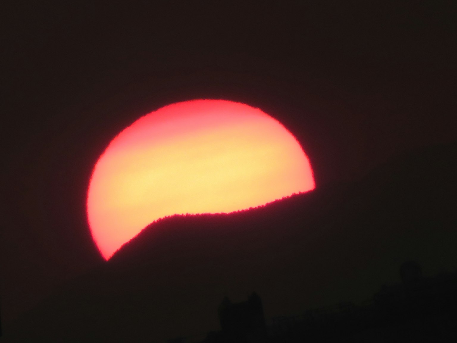 Sole arancione che tramonta dietro una montagna