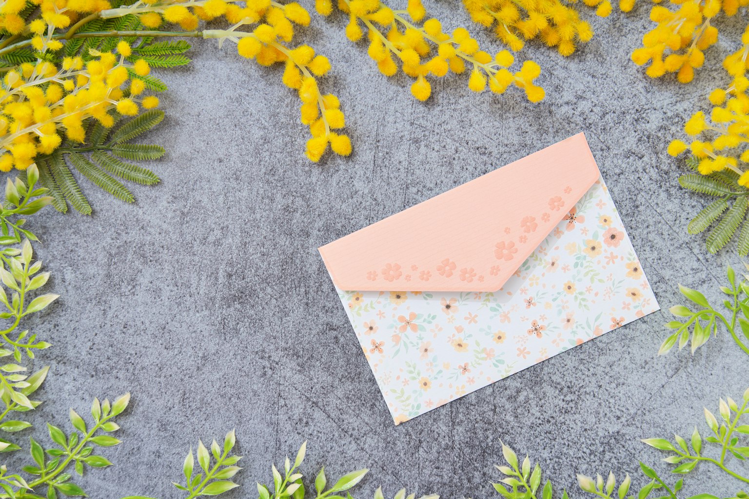 Enveloppe rose entourée de fleurs de mimosa jaunes et de feuilles vertes