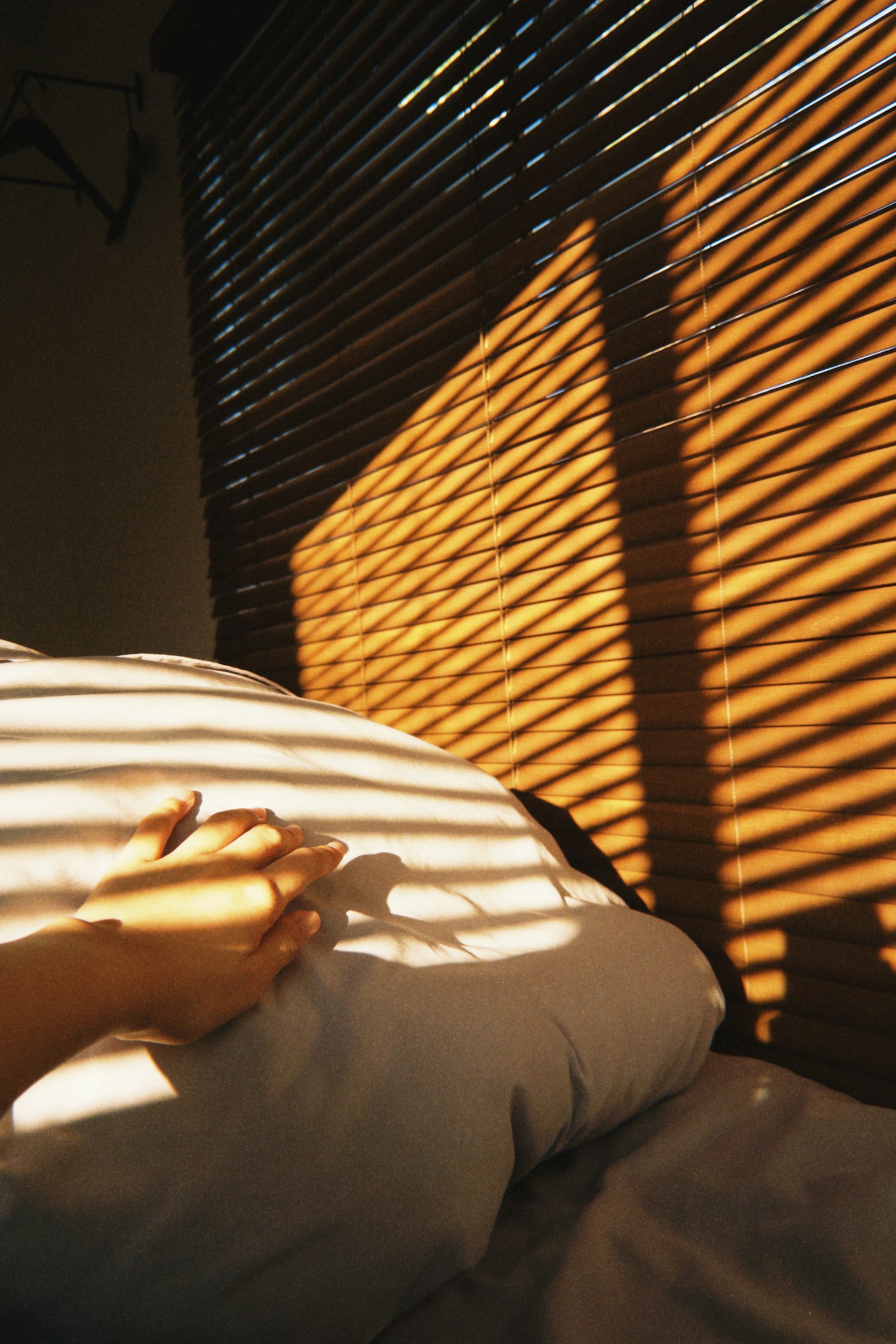 A hand resting on a pillow with shadows from blinds in a cozy bedroom