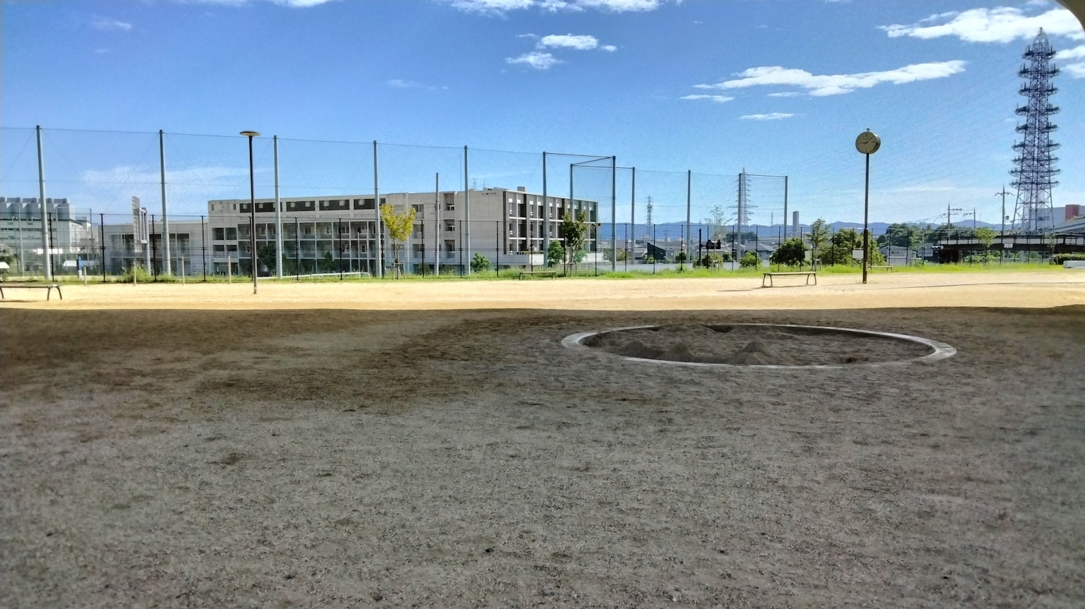 Amplia área de arena de un parque bajo un cielo azul con edificios y redes