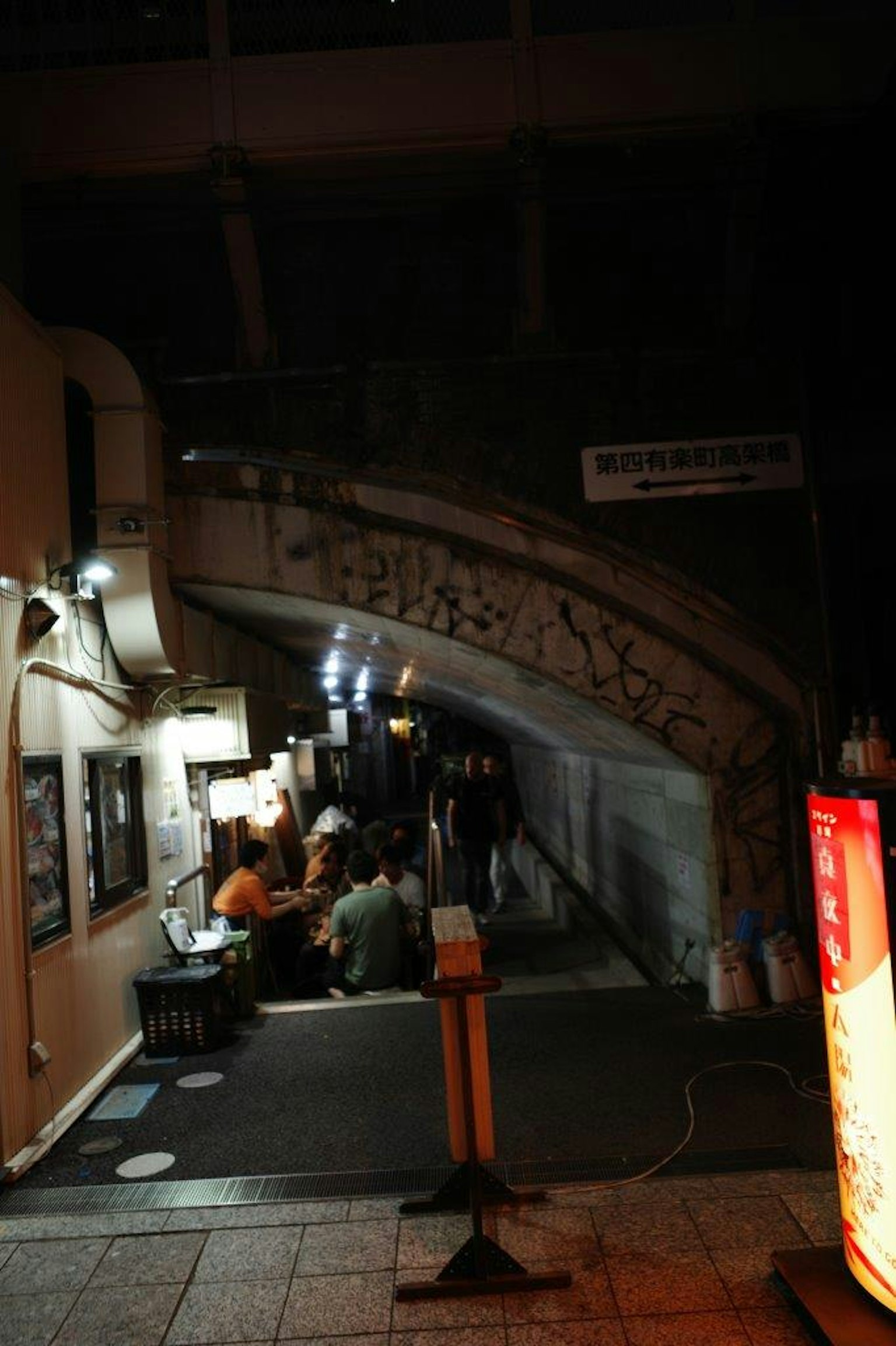 Escena nocturna de restaurantes bajo un puente personas reunidas a lo largo de la calle