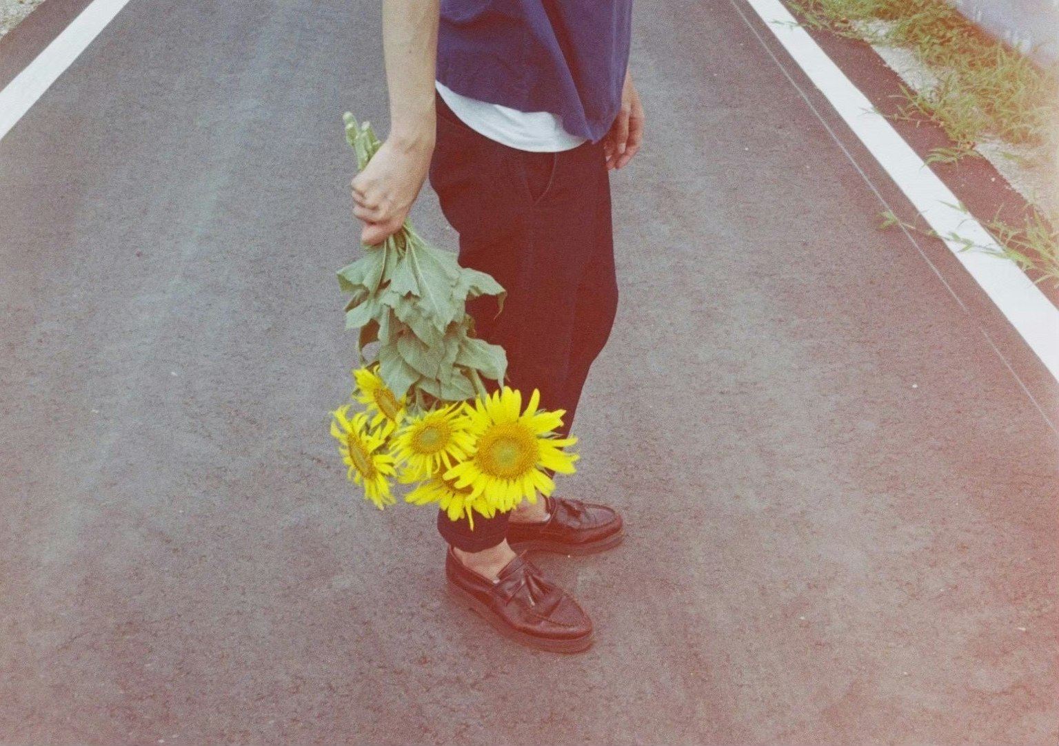 A person holding sunflowers while standing on a road