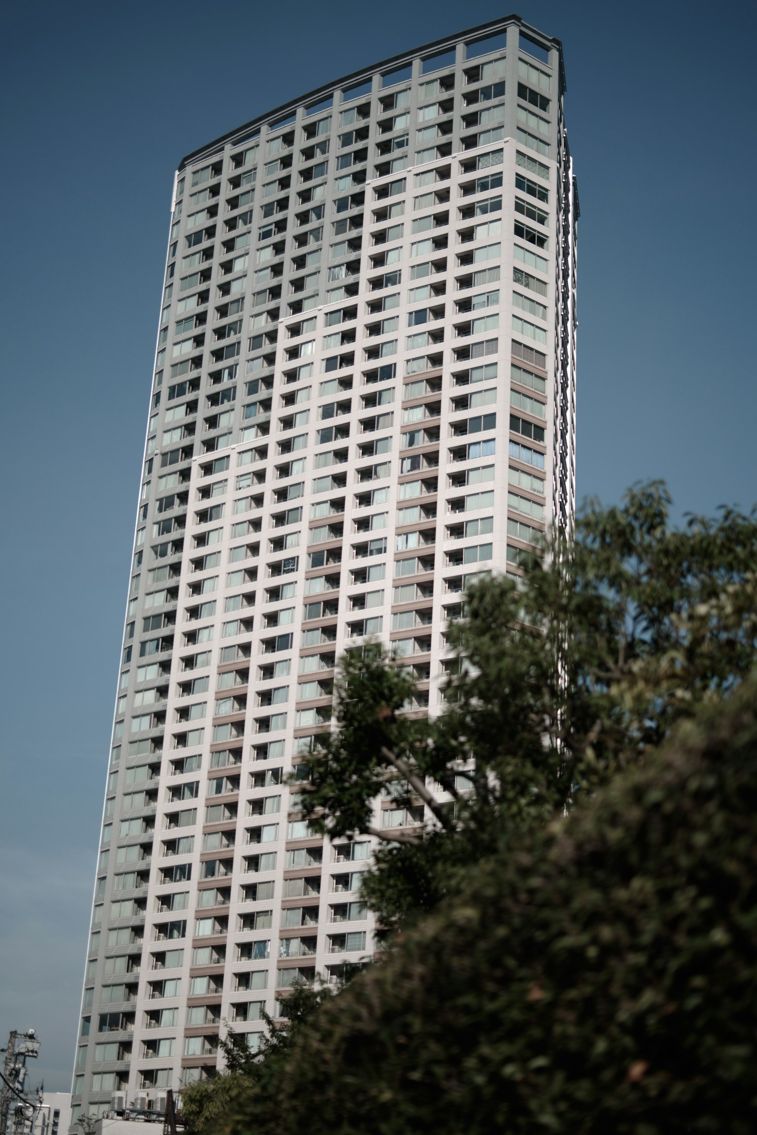 Edificio de gran altura con diseño moderno bajo un cielo azul y árboles verdes