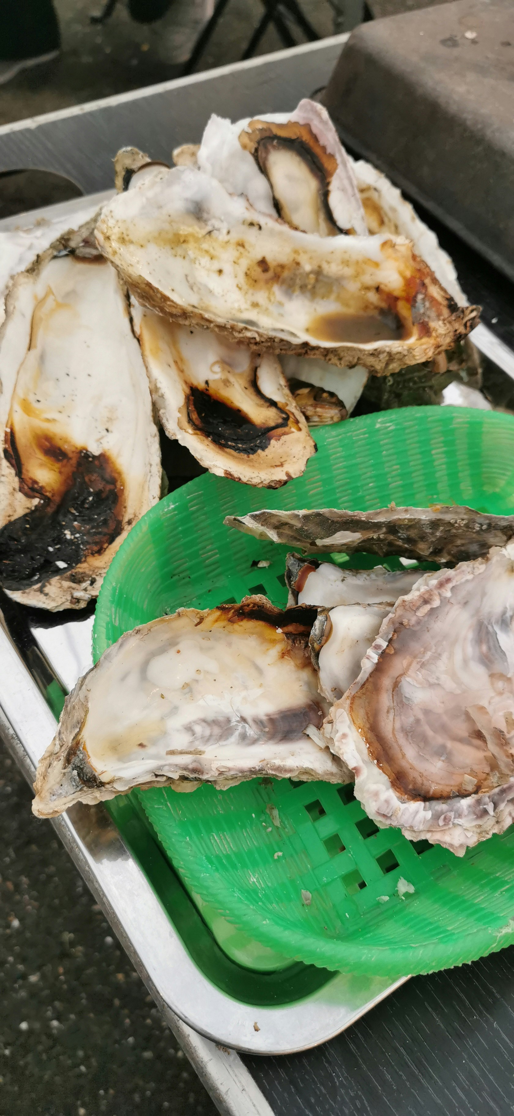 hàu nướng xếp trên khay màu xanh trong không gian quầy ngoài trời