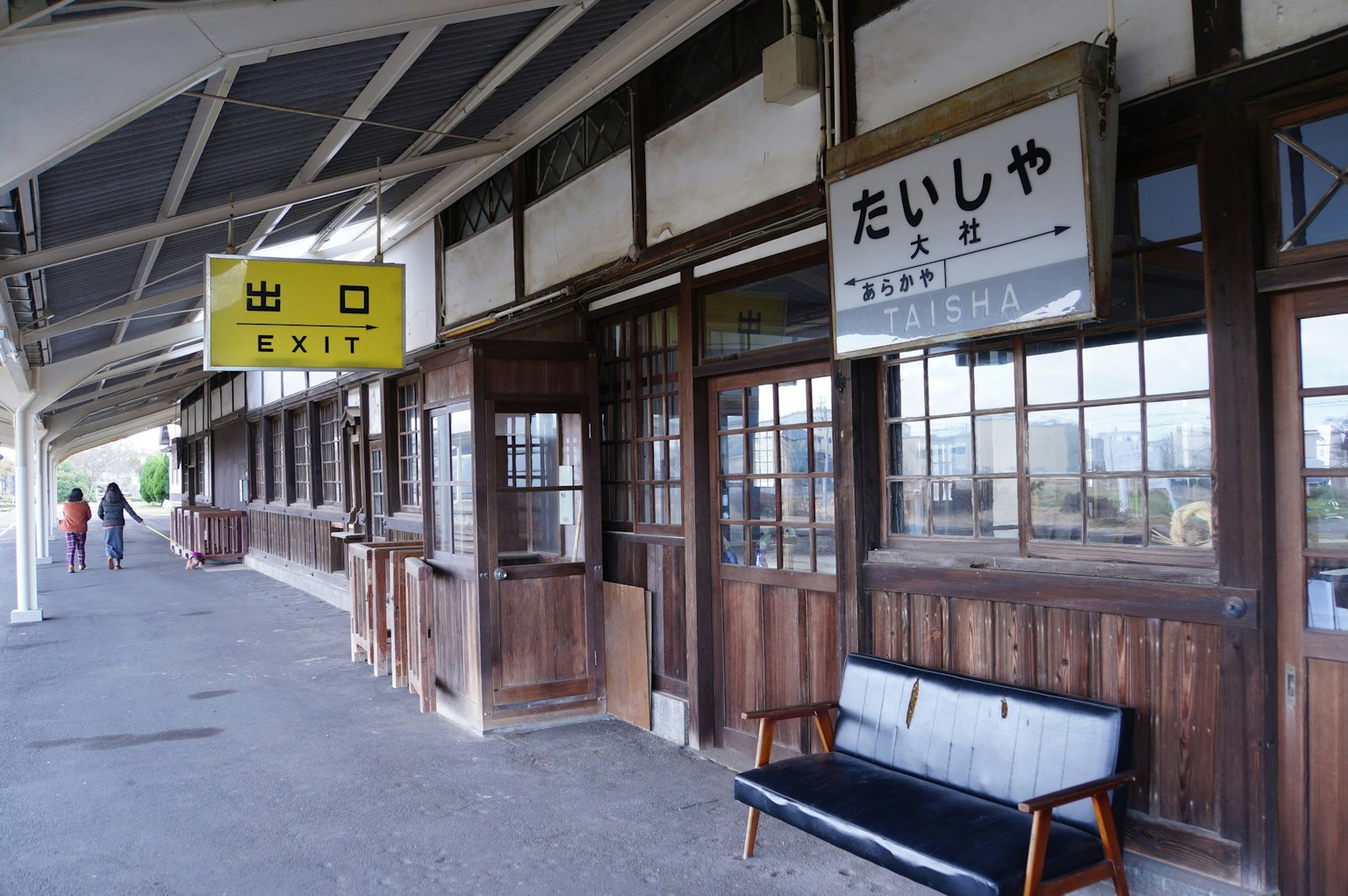 Exterior de una vieja estación de tren con banco de madera y letreros