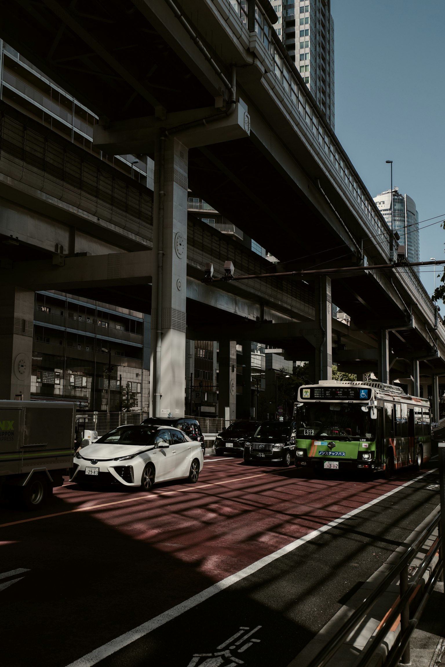 Traffic scene under an elevated road featuring a white car and a green bus in an urban setting