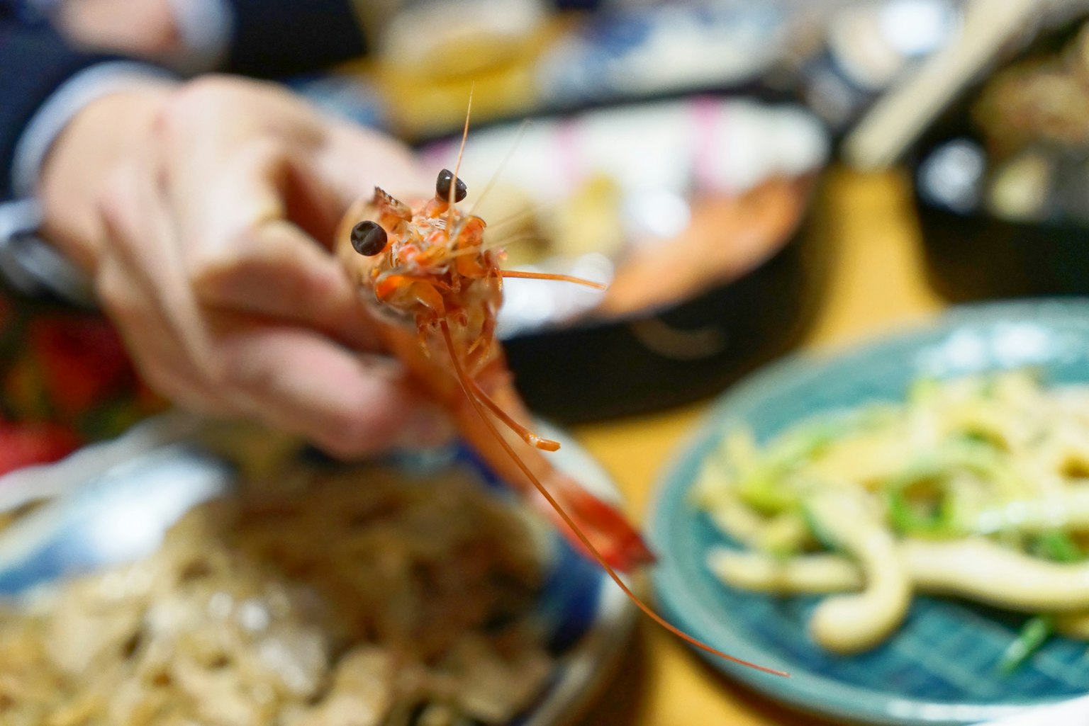 手中握着新鲜虾，背景是传统日本菜肴
