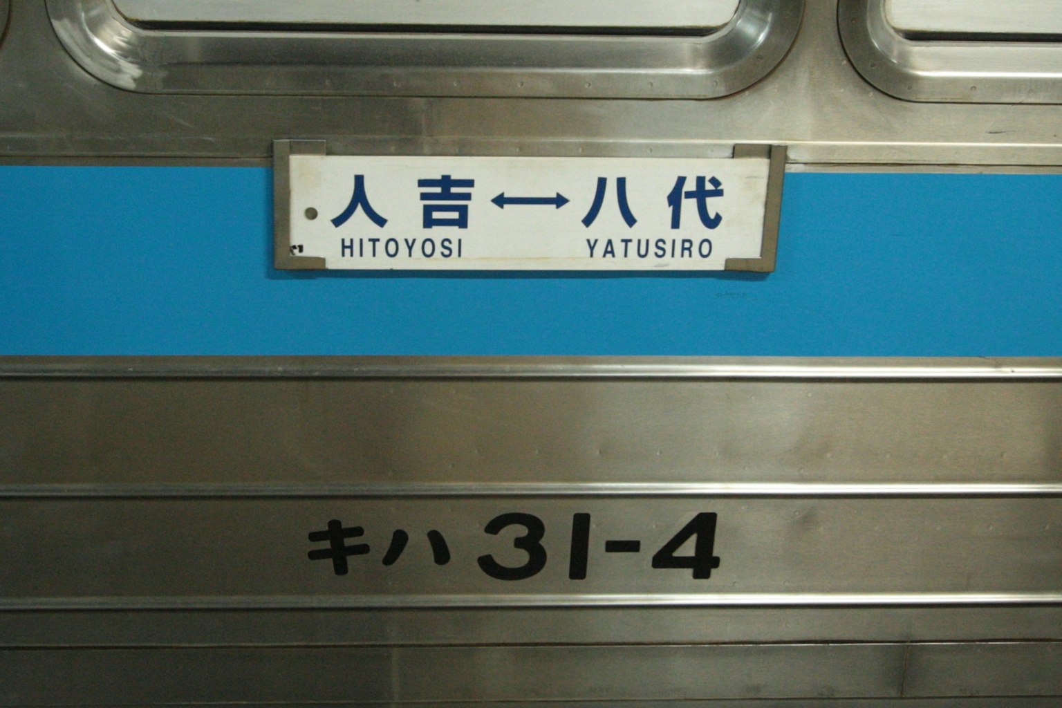 Cartel en el lateral de un vagón de tren con una franja azul y el texto Hitoyoshi Yatsushiro