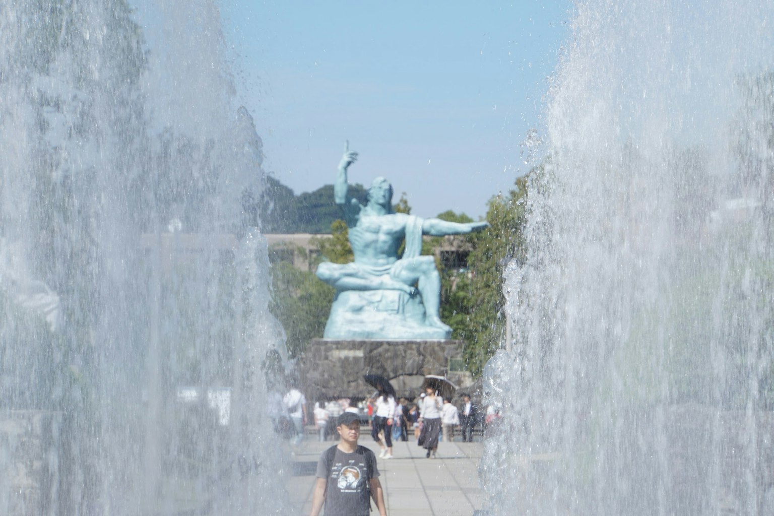 Personas caminando frente a una estatua de bronce con fuentes en primer plano