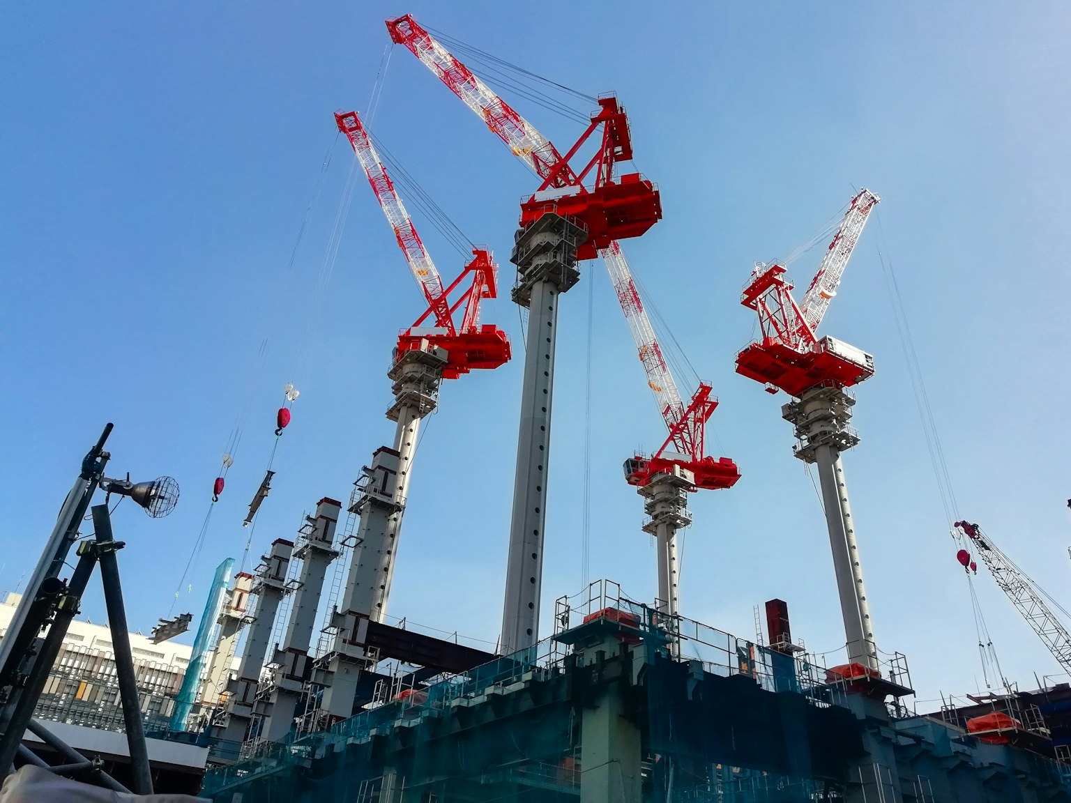 Situs konstruksi dengan beberapa crane merah di bawah langit biru yang cerah