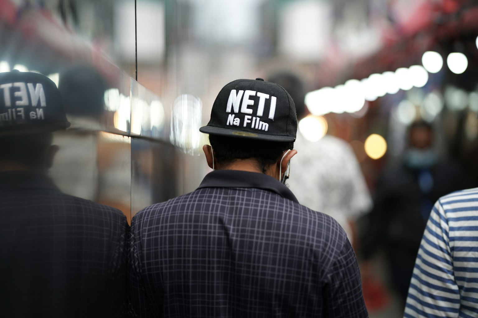 ผู้ชายที่สวมหมวกเขียนว่า NETI in Film มองจากด้านหลัง