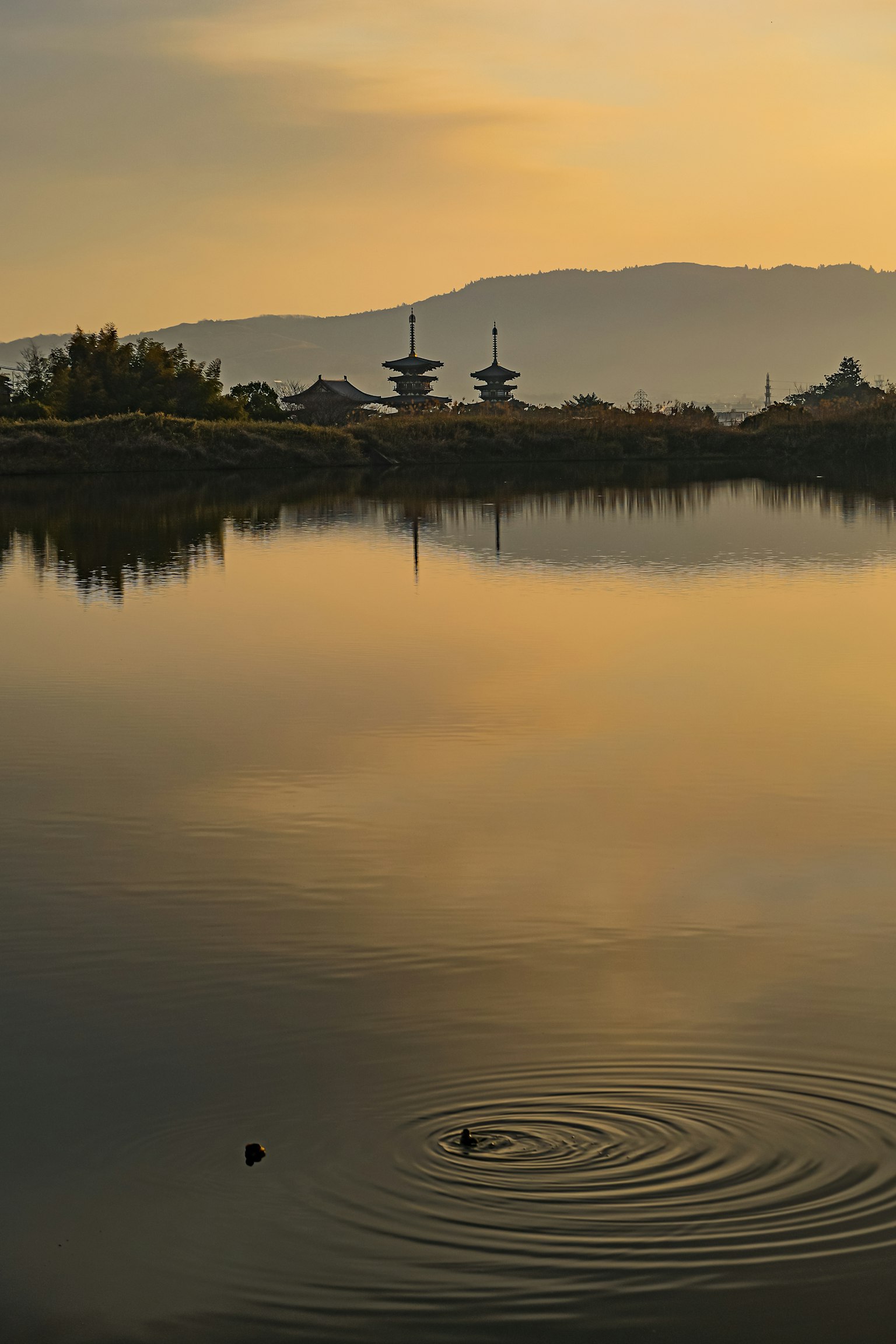 Lago tranquilo reflejando el atardecer y las siluetas de las montañas