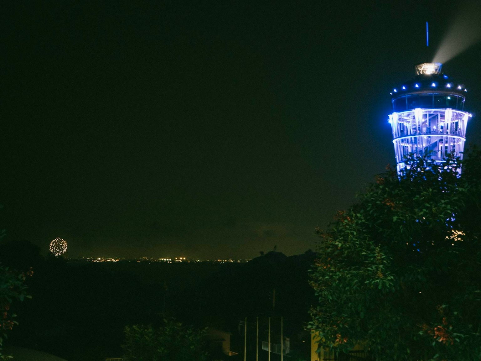 A tower emitting blue light at night with distant city lights