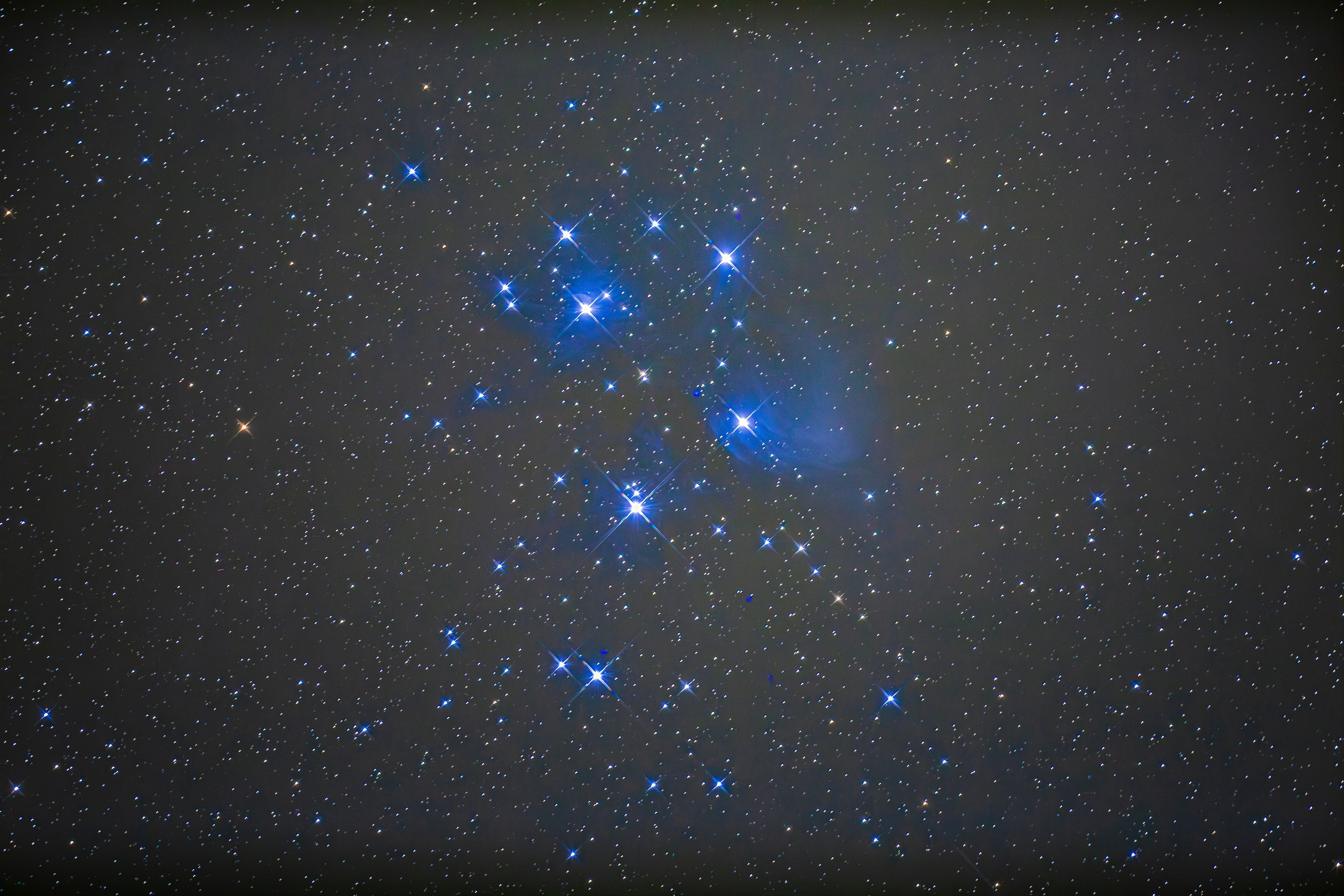 Cluster of bright blue stars in the night sky with nebula