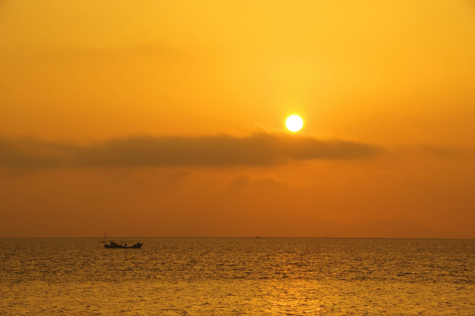 Beautiful sunset over the ocean with a small boat drifting